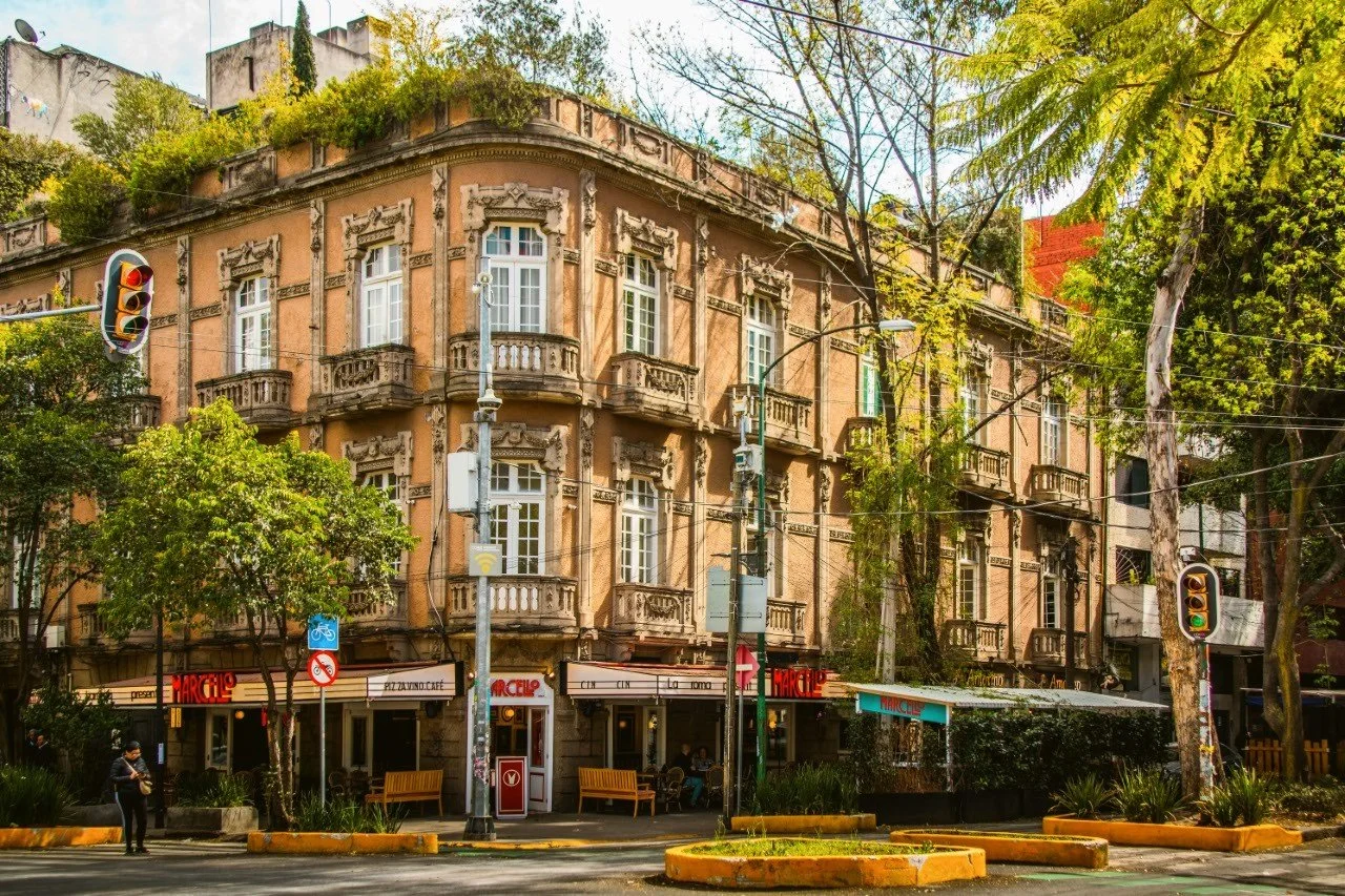 Elegant apartment building with balconies and trees along a tree-lined street, Mexico City.