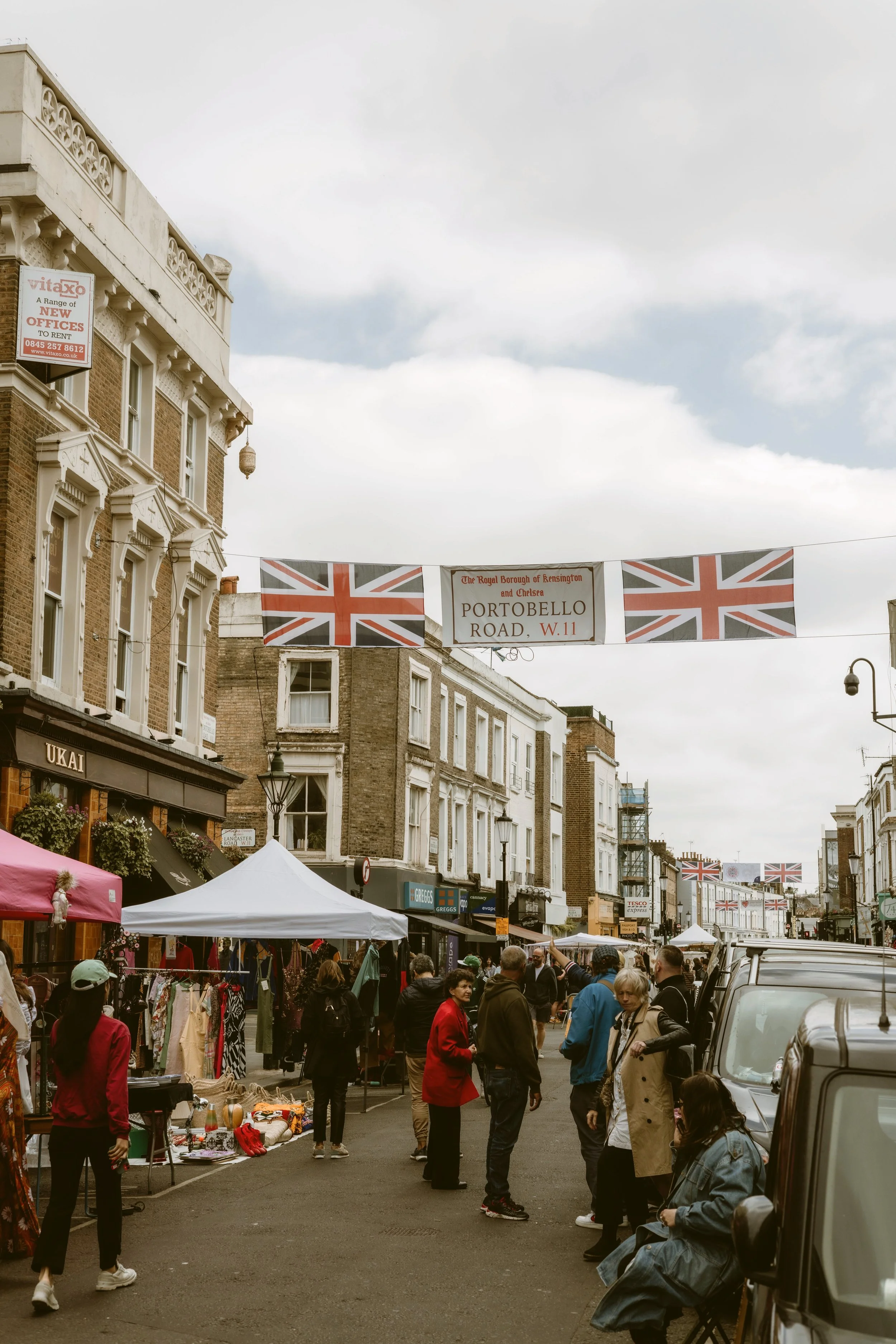 Street market with stalls and pastel-colored buildings on Portobello Road, London.