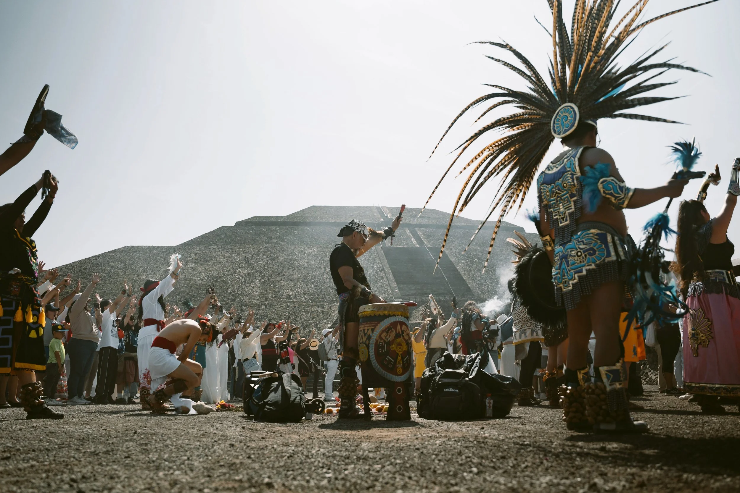 Dancers in feathered headdresses and drummers performing outdoors with hills in the background, Teotihuacán, Mexico.