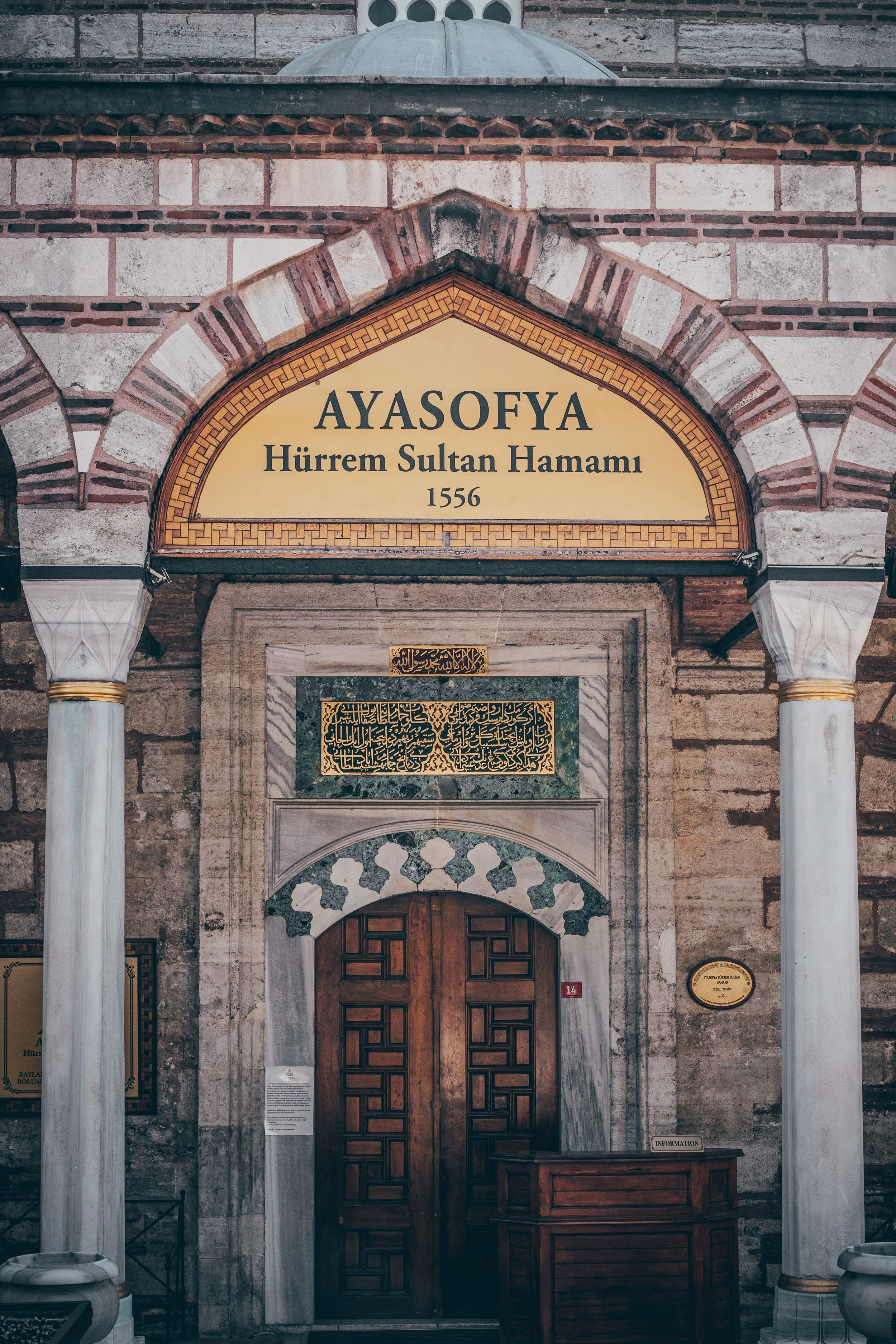 Ornate arched entrance of a historic hamam with striped stonework and a lit doorway, Istanbul.