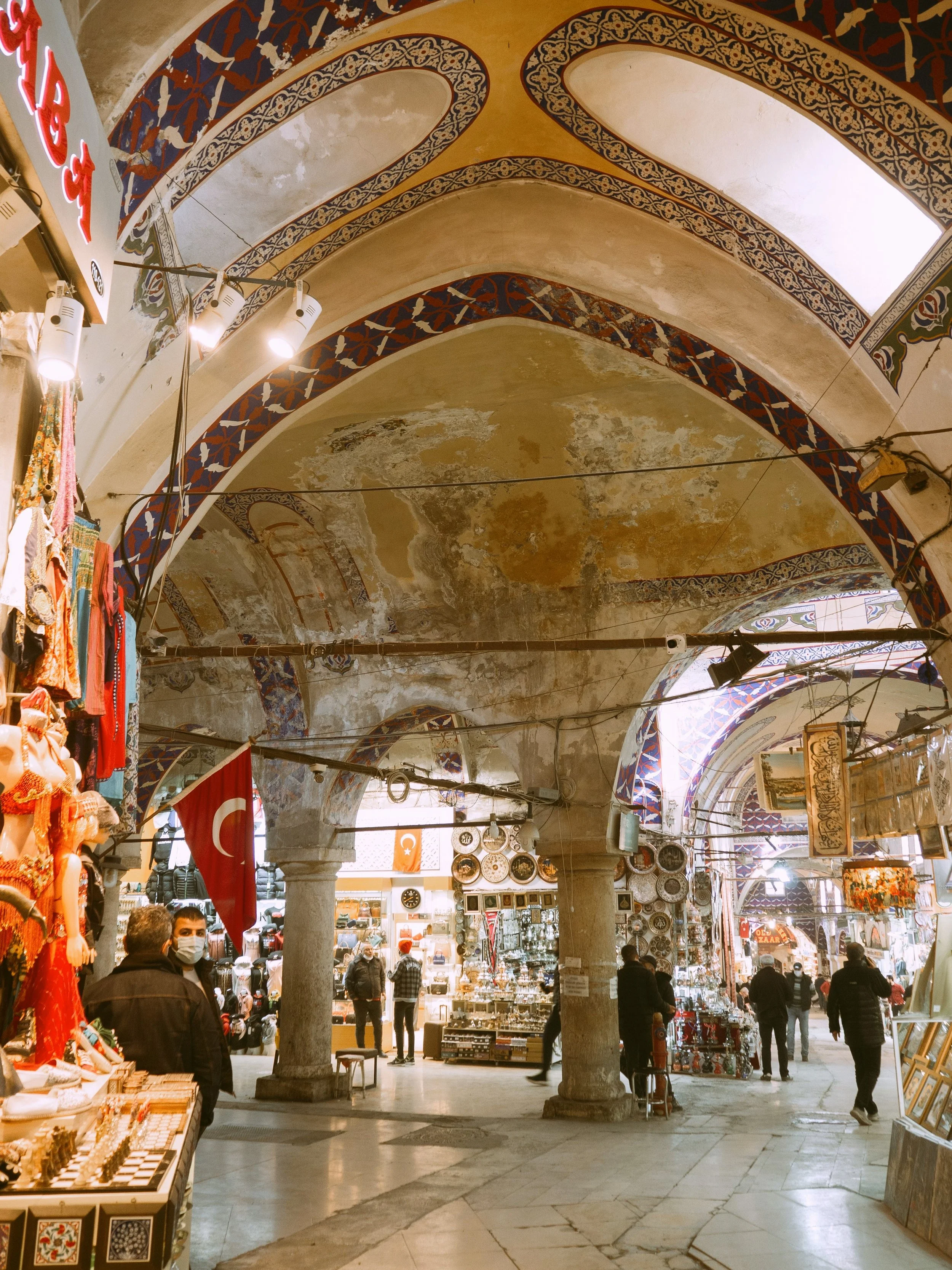 Grand Bazaar covered hall with painted vaulted ceilings, shops on both sides and visitors walking through, Istanbul.