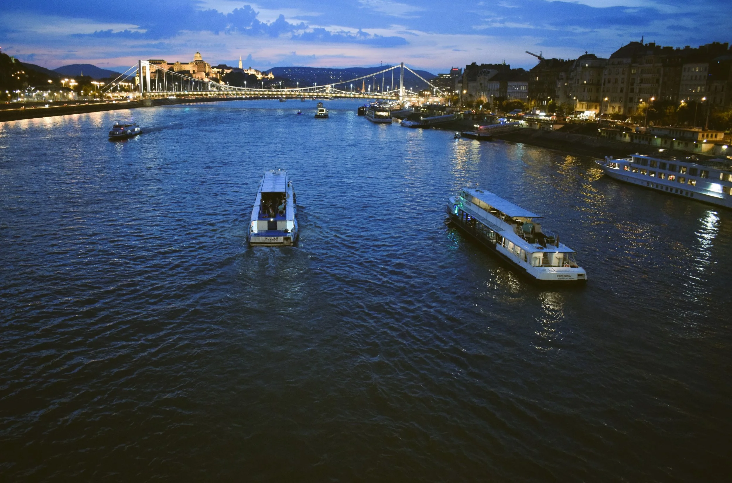 Cruise boats on the Danube at dusk with lit Buda Castle Hill behind, Budapest