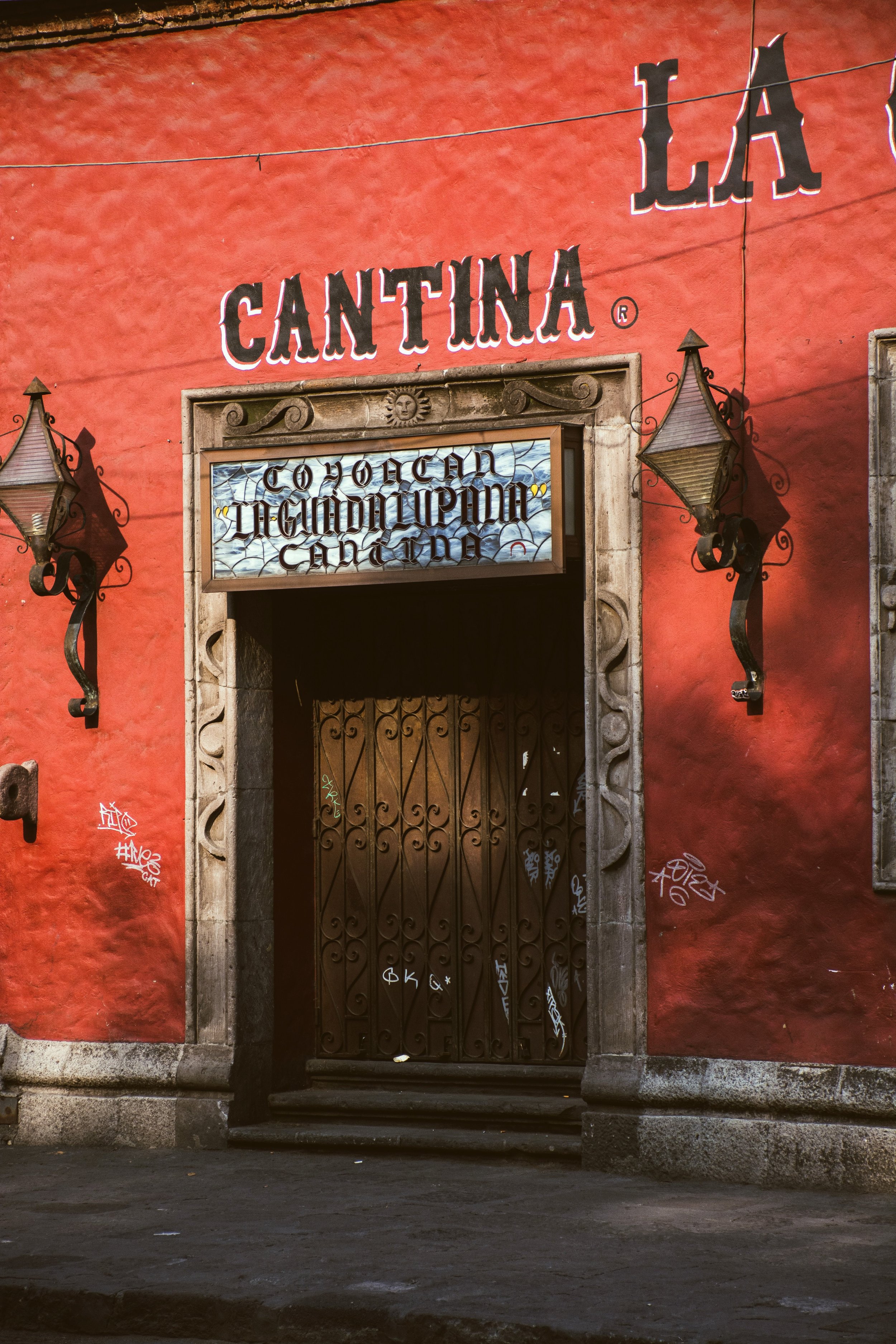 Red facade of a traditional cantina with a wooden door and a sign above the entrance, Mexico City.
