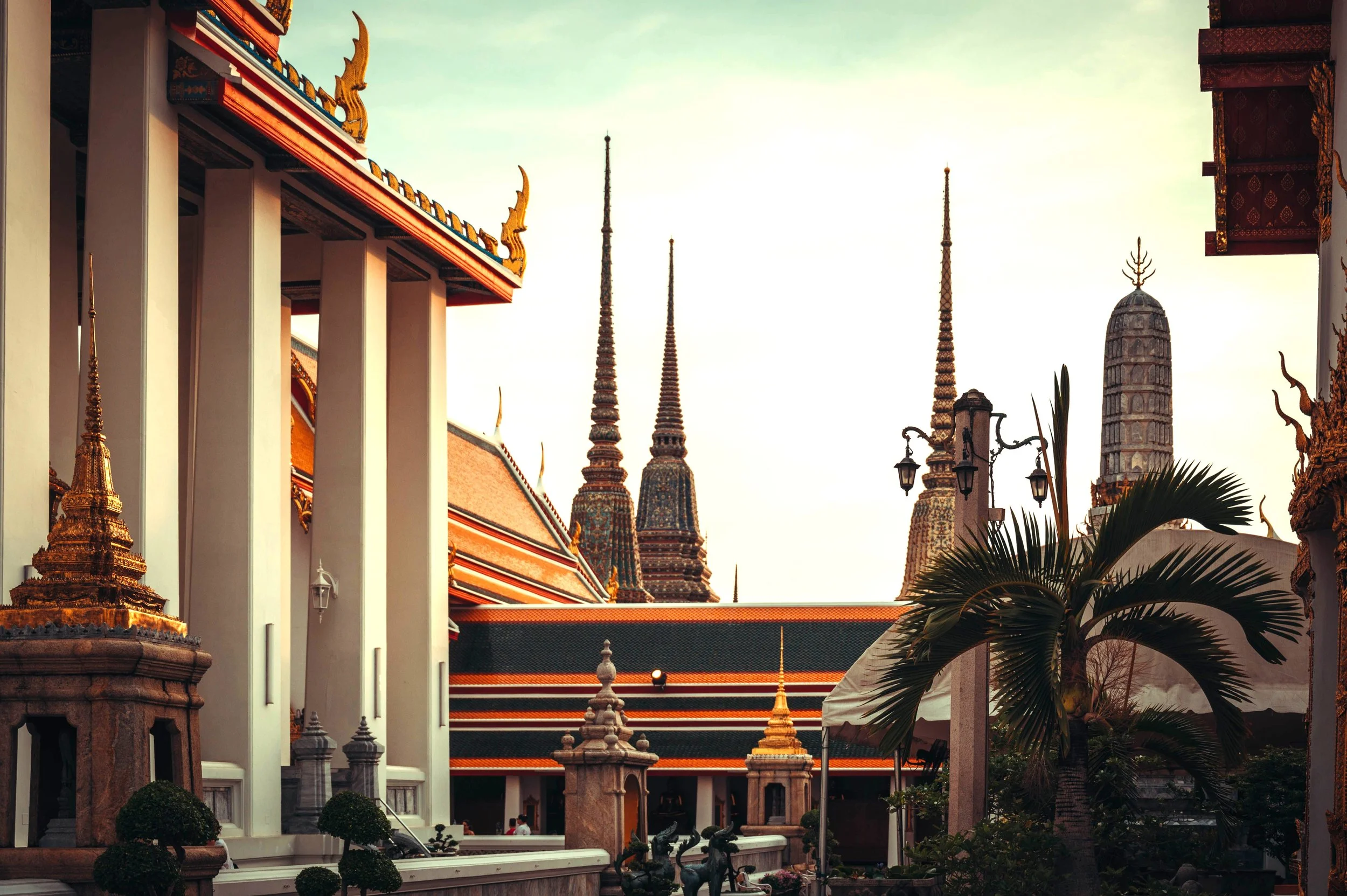 Temple courtyard with white columns, orange tiled roofs and tall spires in the background, Wat Pho, Bangkok.
