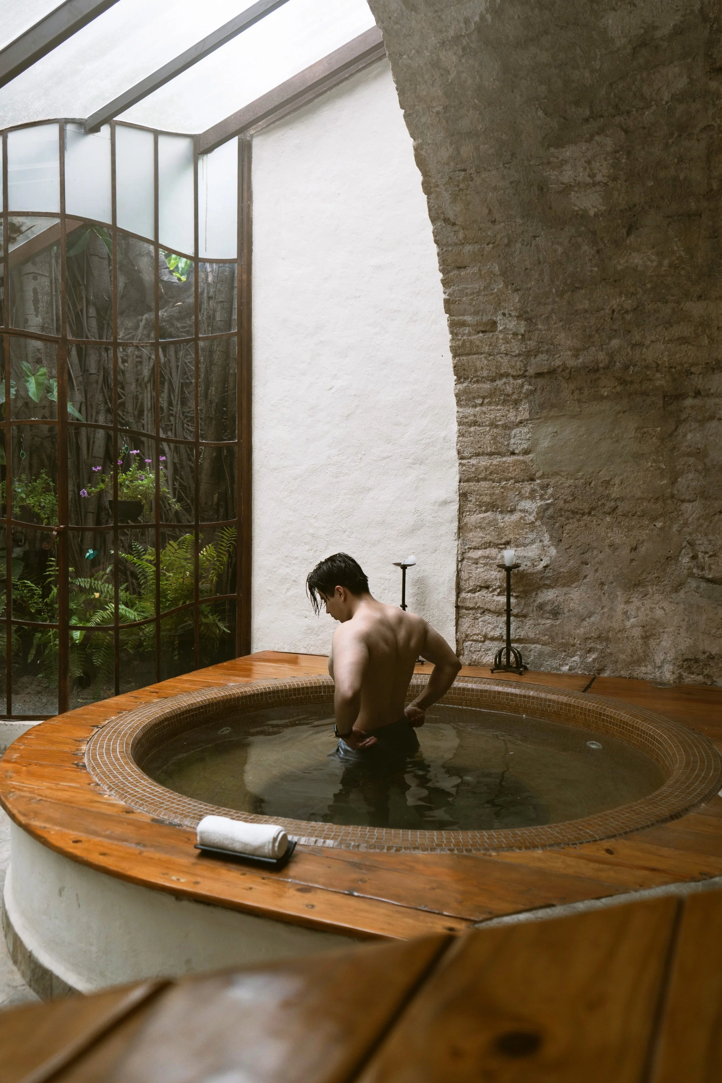 Person soaking in a round wooden onsen bath beside a stone wall and small garden, Japan.