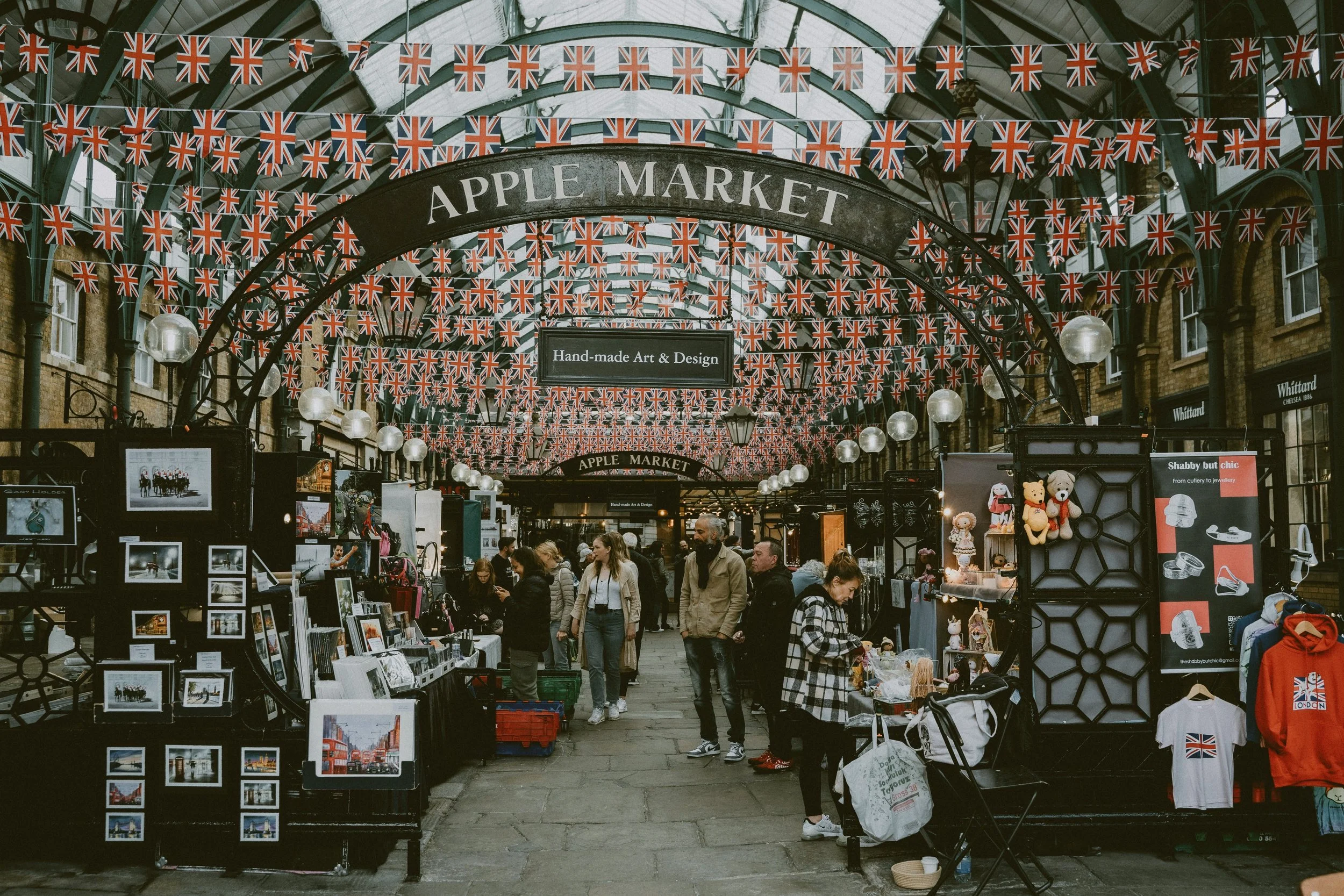 Covered market hall with stalls, hanging bunting and visitors browsing, London