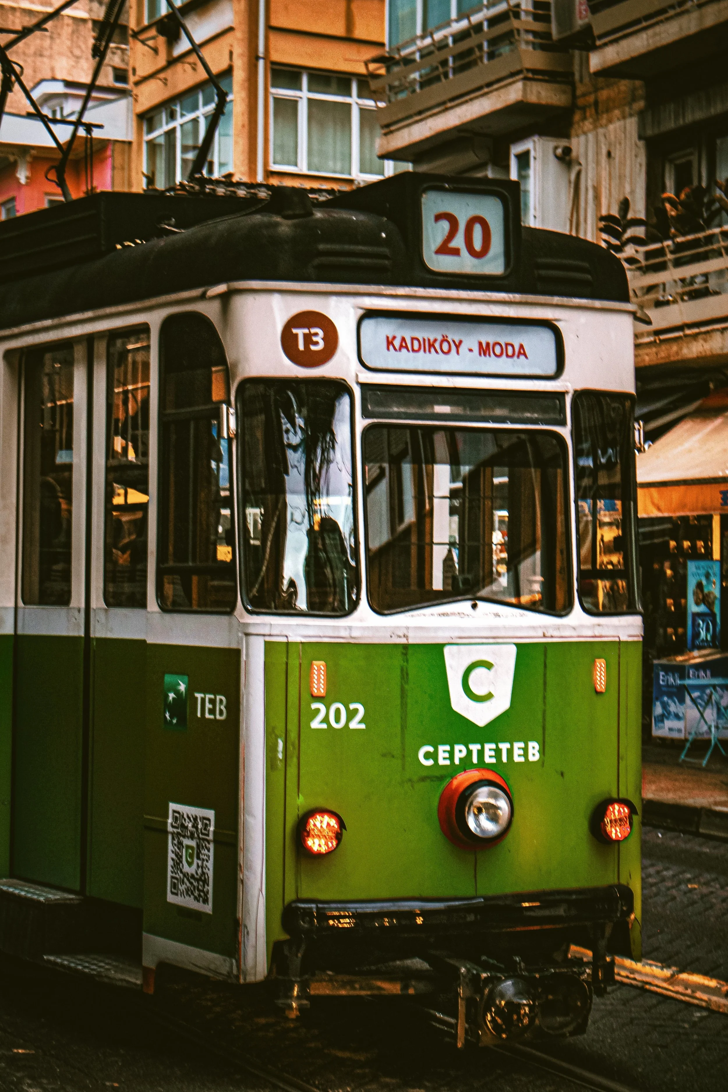 Green vintage tram passing in front of an illuminated building at dusk, Kadikoy, Istanbul.