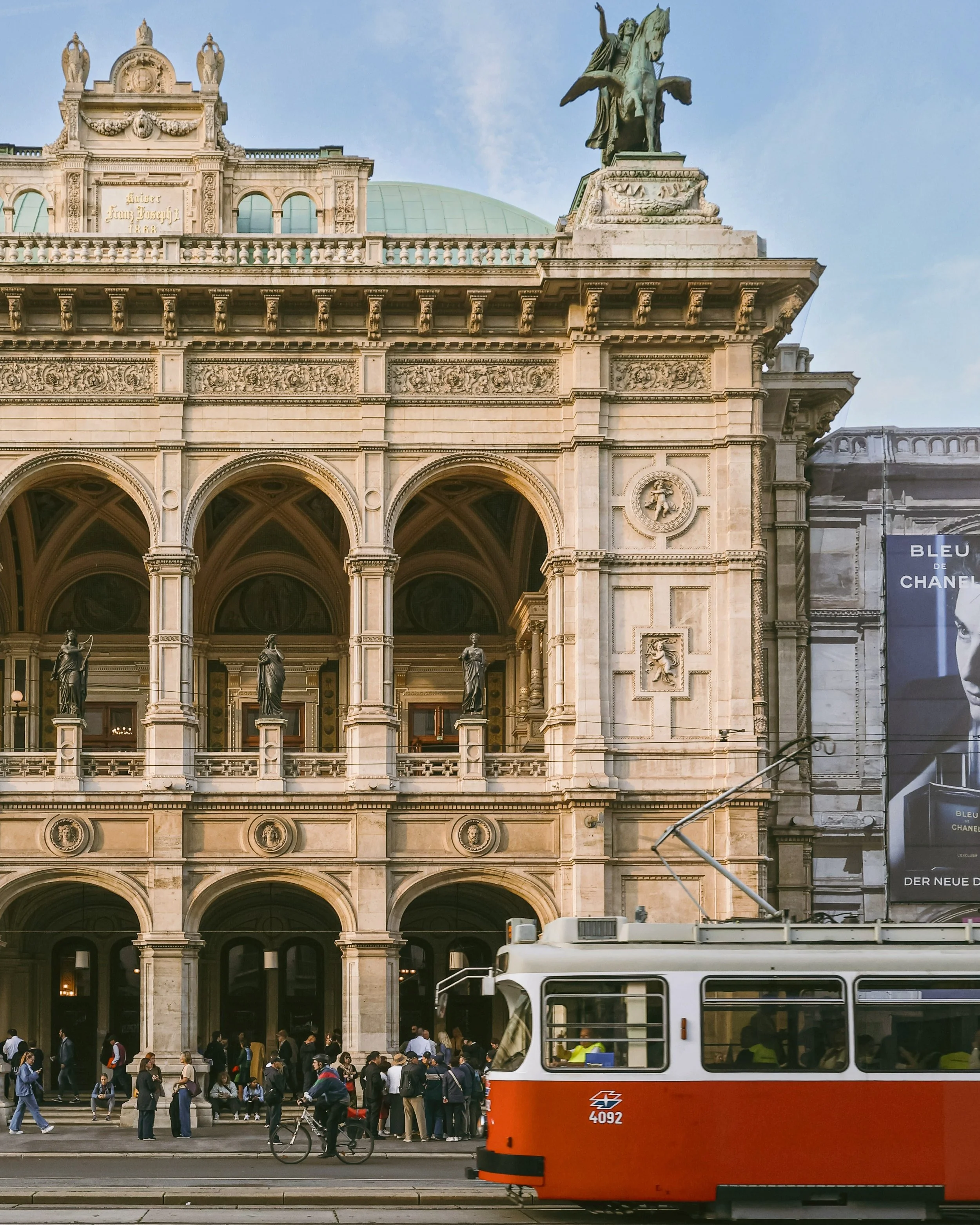 Red tram passing the Vienna State Opera facade with its statue-topped loggia, Ringstrasse, Vienna.
