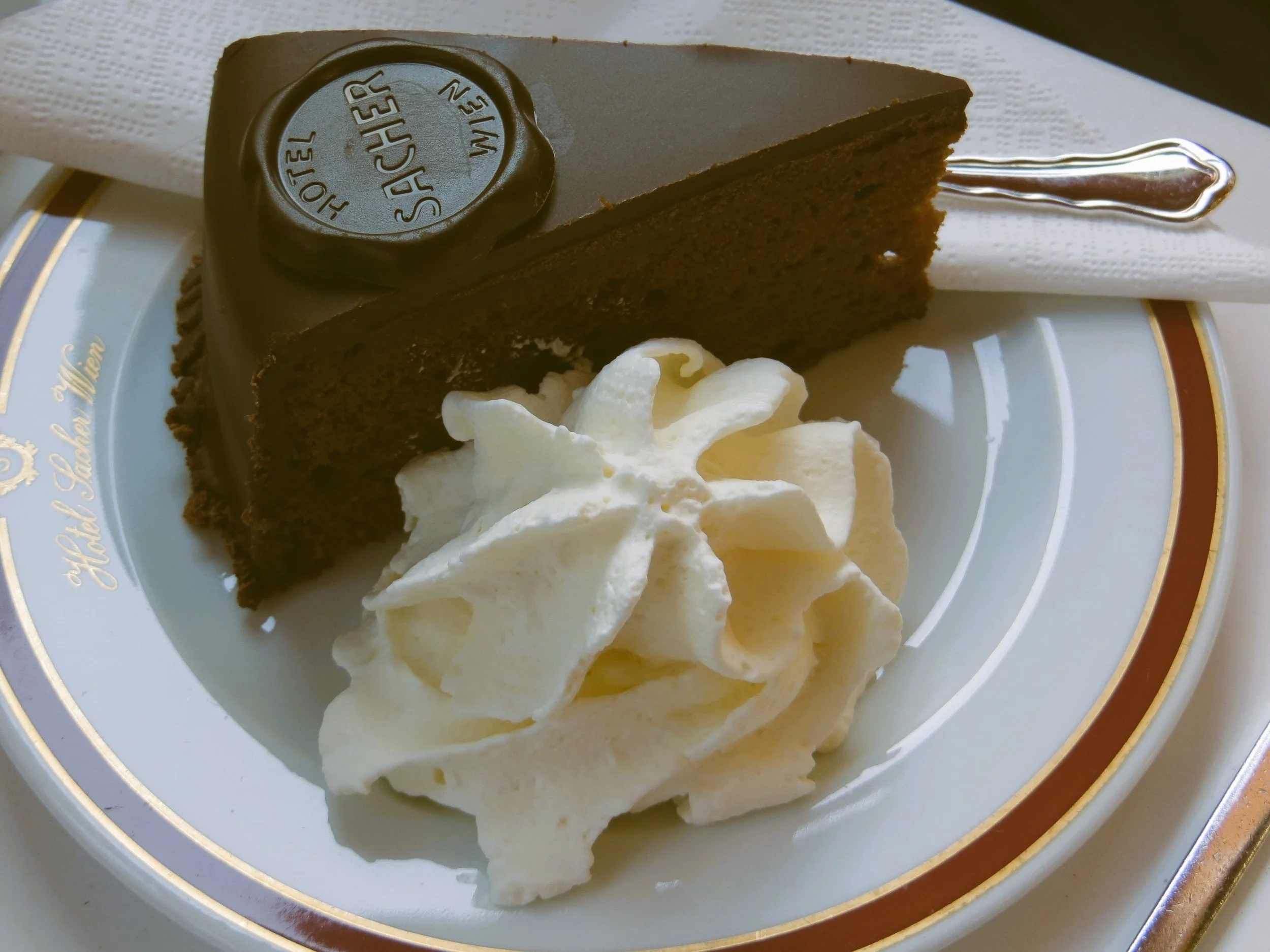 Slice of Sachertorte with a dollop of whipped cream on a white plate with a red rim, Vienna.