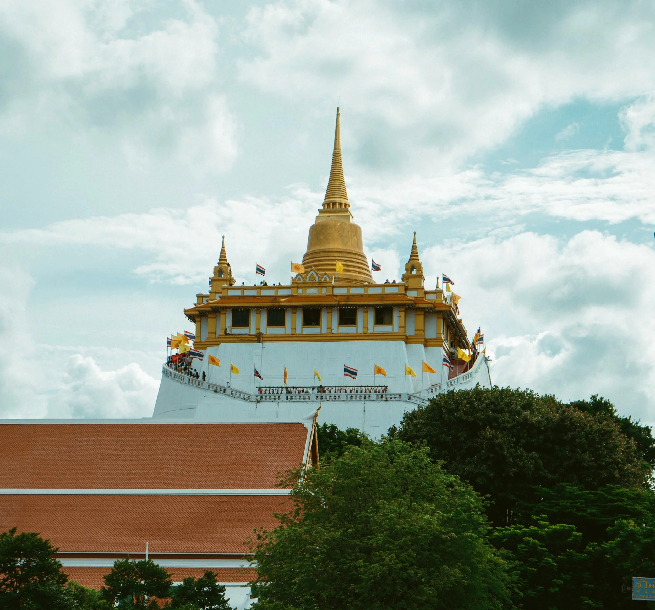 Golden chedi on top of a white hill temple rising above trees and orange tiled roofs, Wat Saket (Golden Mount), Bangkok.