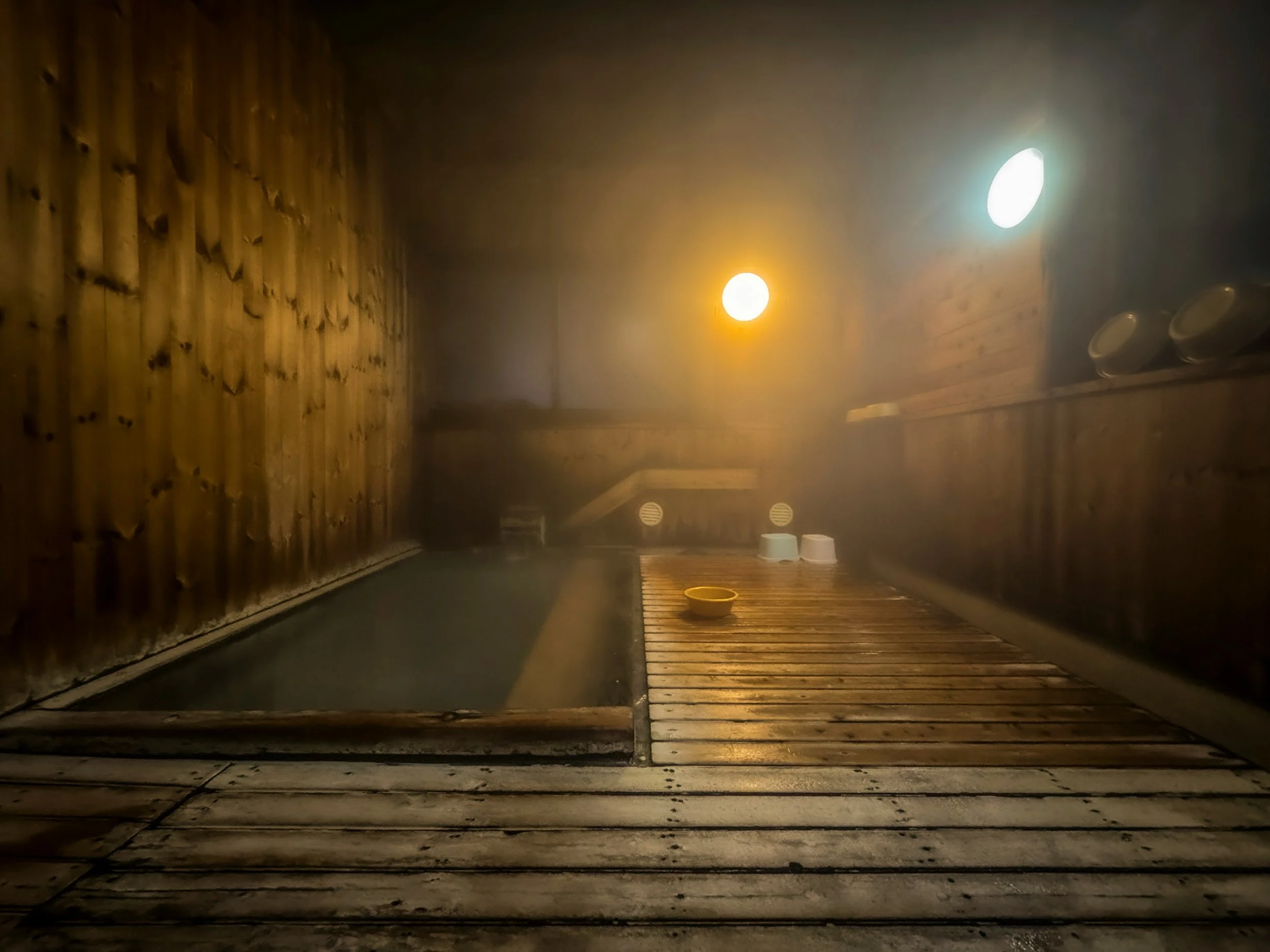 Steaming wooden onsen bath with warm light glowing through the mist, Japan.
