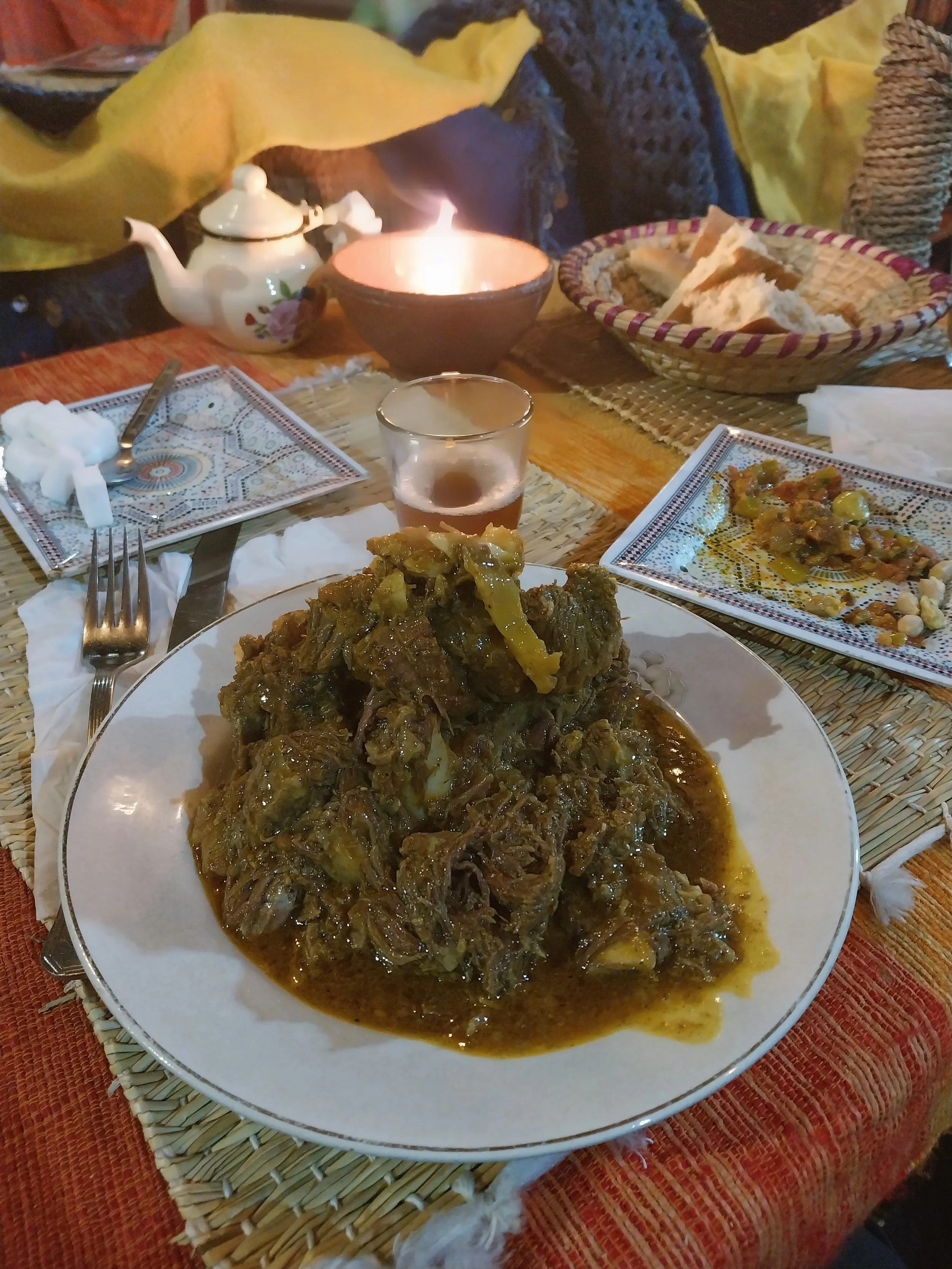 Tanjia of slow-cooked shredded meat on a white plate with small salad dishes and a glass of mint tea, Marrakech