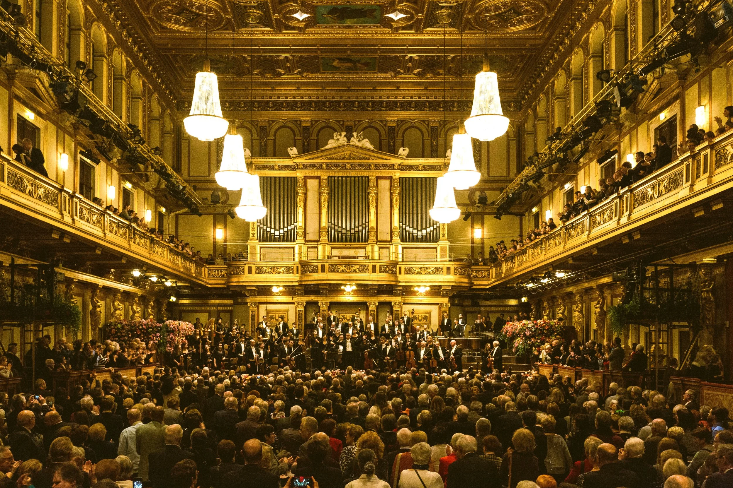 New Year's Concert in the gilded Musikverein hall, with the orchestra on stage before a packed audience and flower arrangements, Vienna