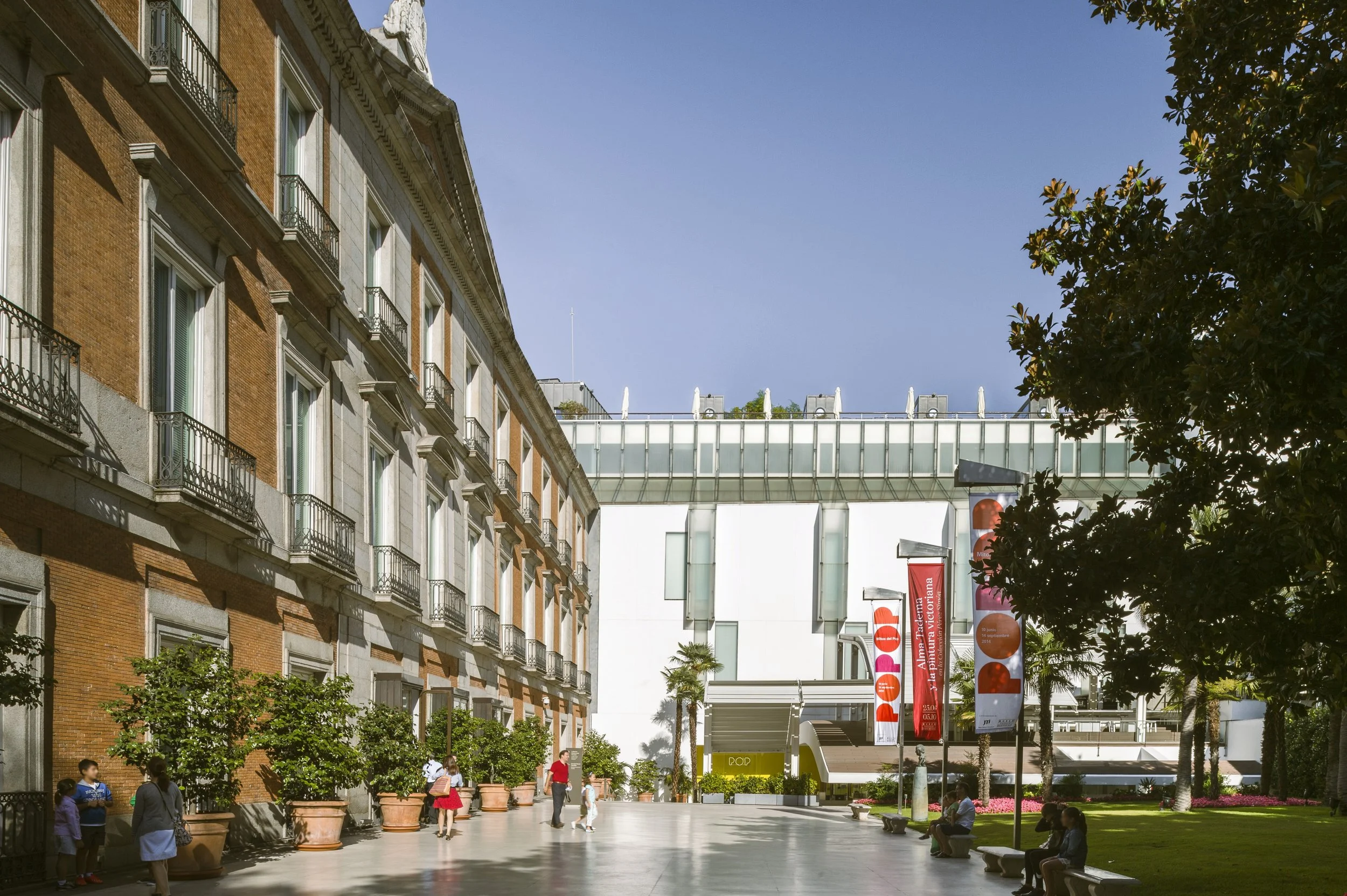 Thyssen-Bornemisza Museum brick facade beside its modern white extension and a garden with banners, Madrid