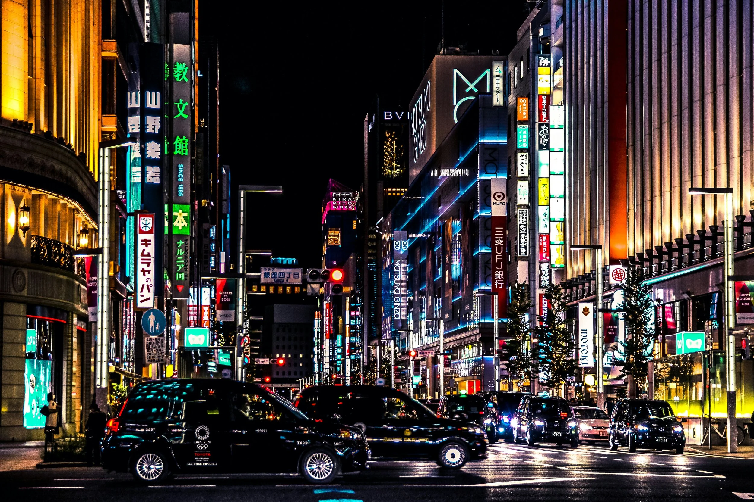 Taxis on a street at night lined with illuminated signs and neon-lit buildings, Ginza, Tokyo.