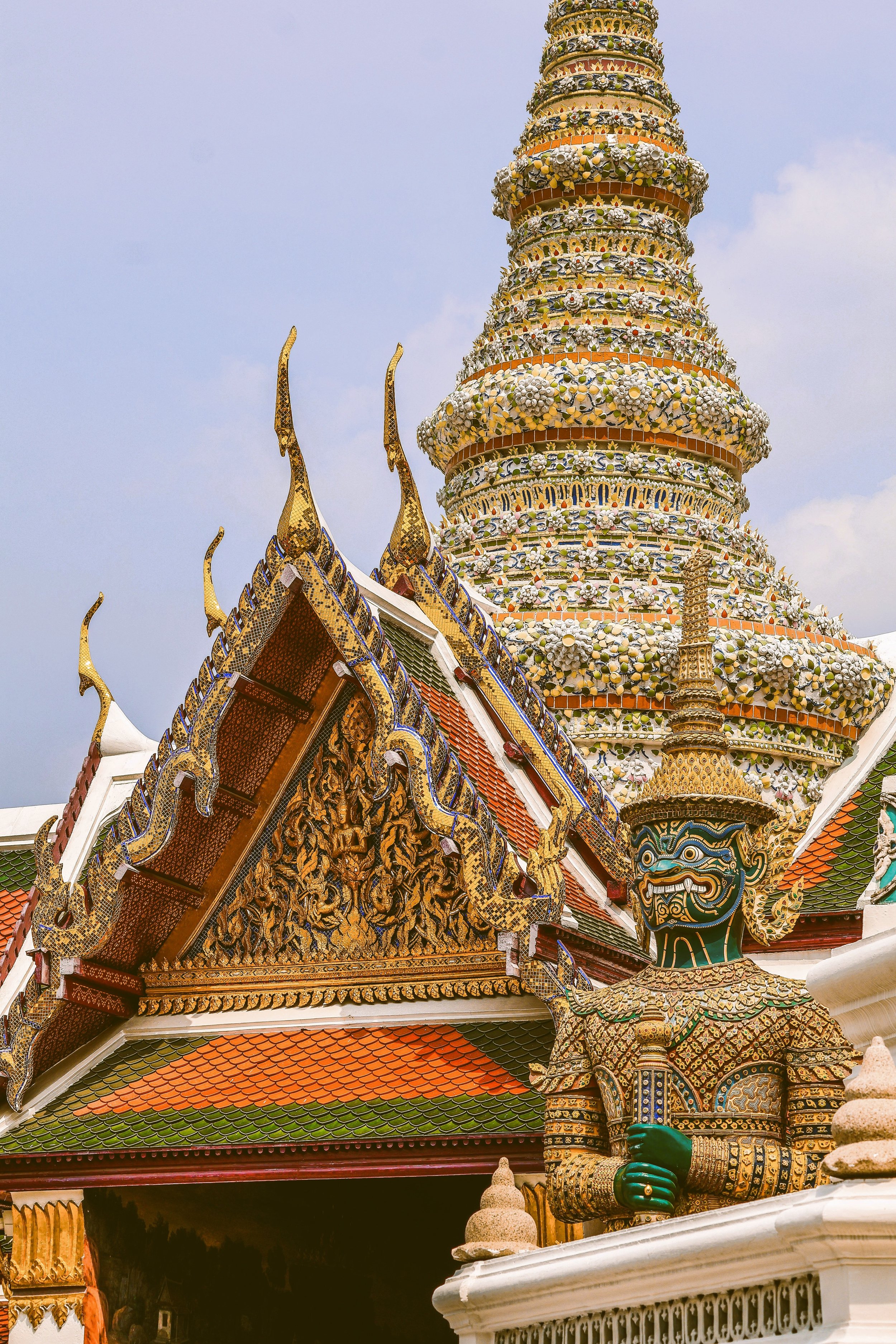 Ornate temple roof with a gilded spire rising above it against a blue sky, Grand Palace, Bangkok.