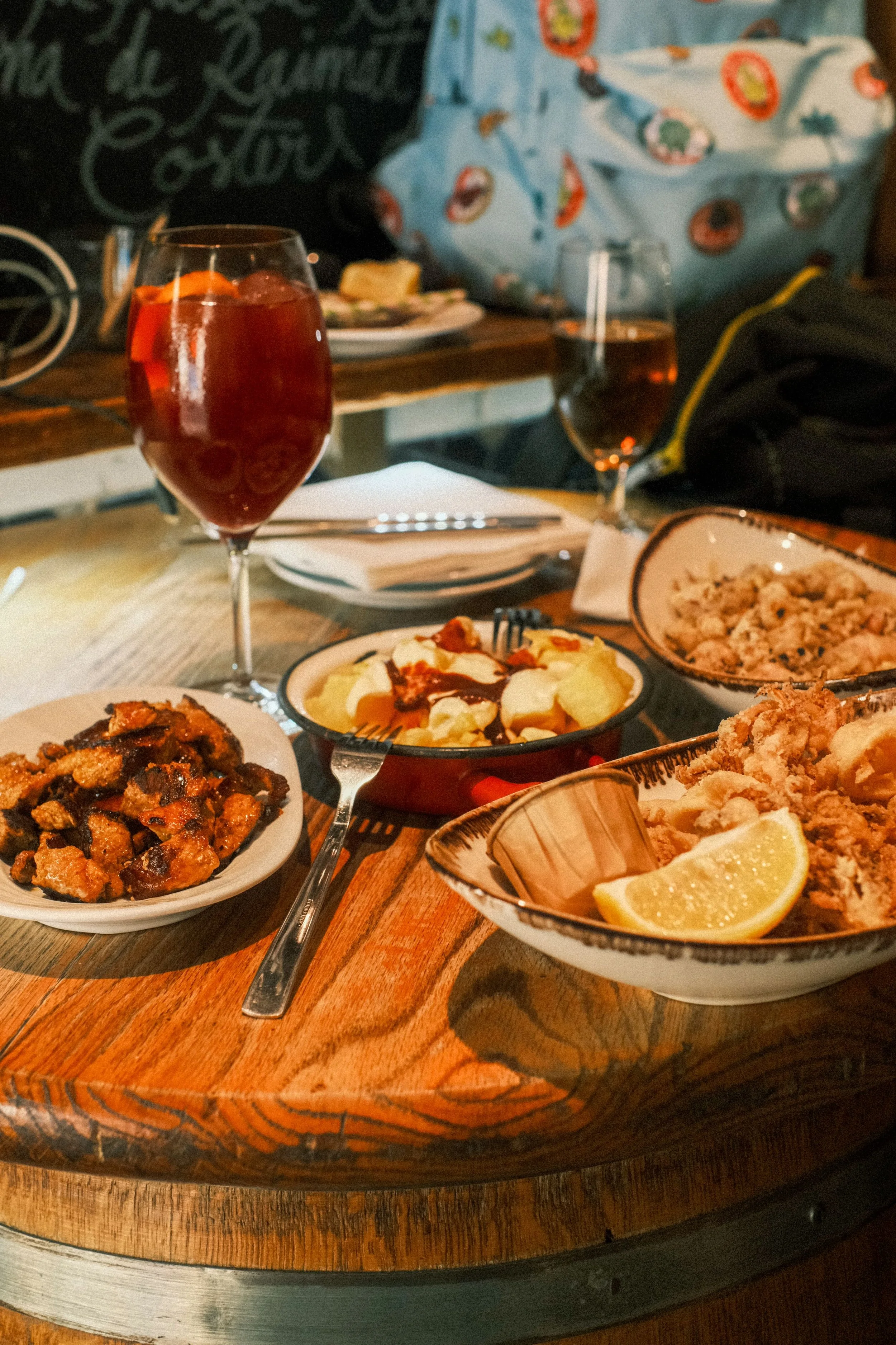 Plates of tapas and a glass of vermouth on a wooden barrel table, Madrid