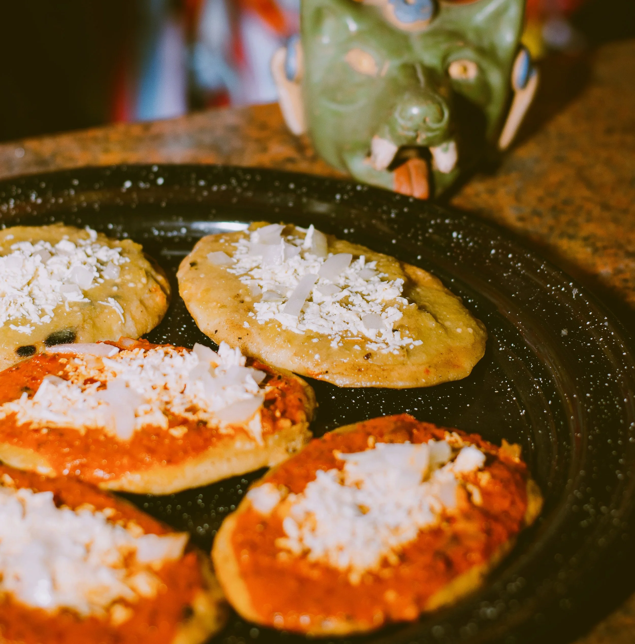 Tlacoyos topped with salsa and cheese on a dark clay comal, Mexico City.