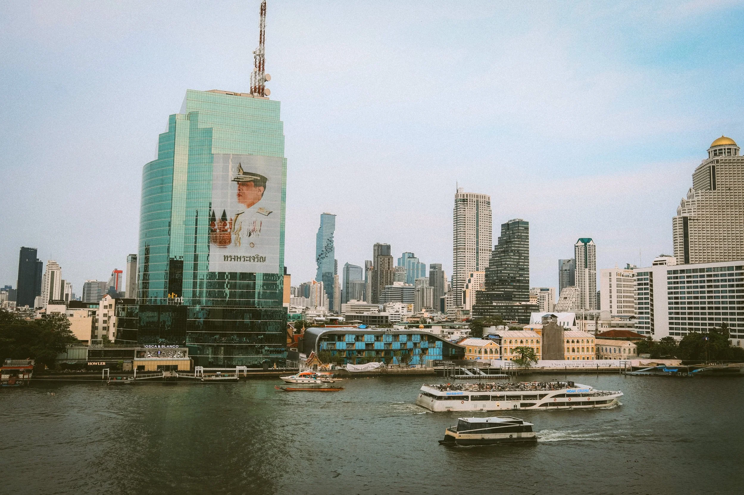 Chao Phraya River with boats and the city skyline of glass towers along the bank, Bangkok.