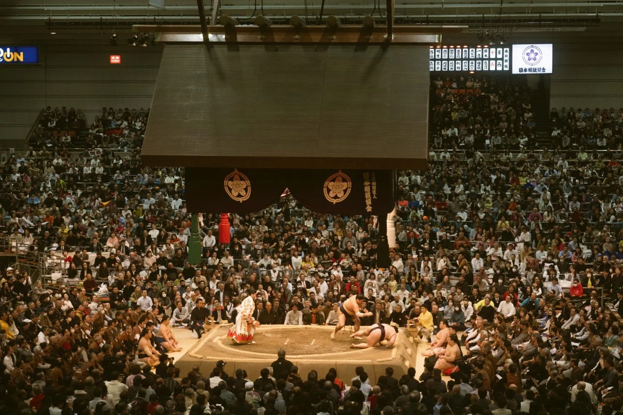 A large sumo wrestling match taking place in an arena filled with spectators, Tokyo.
