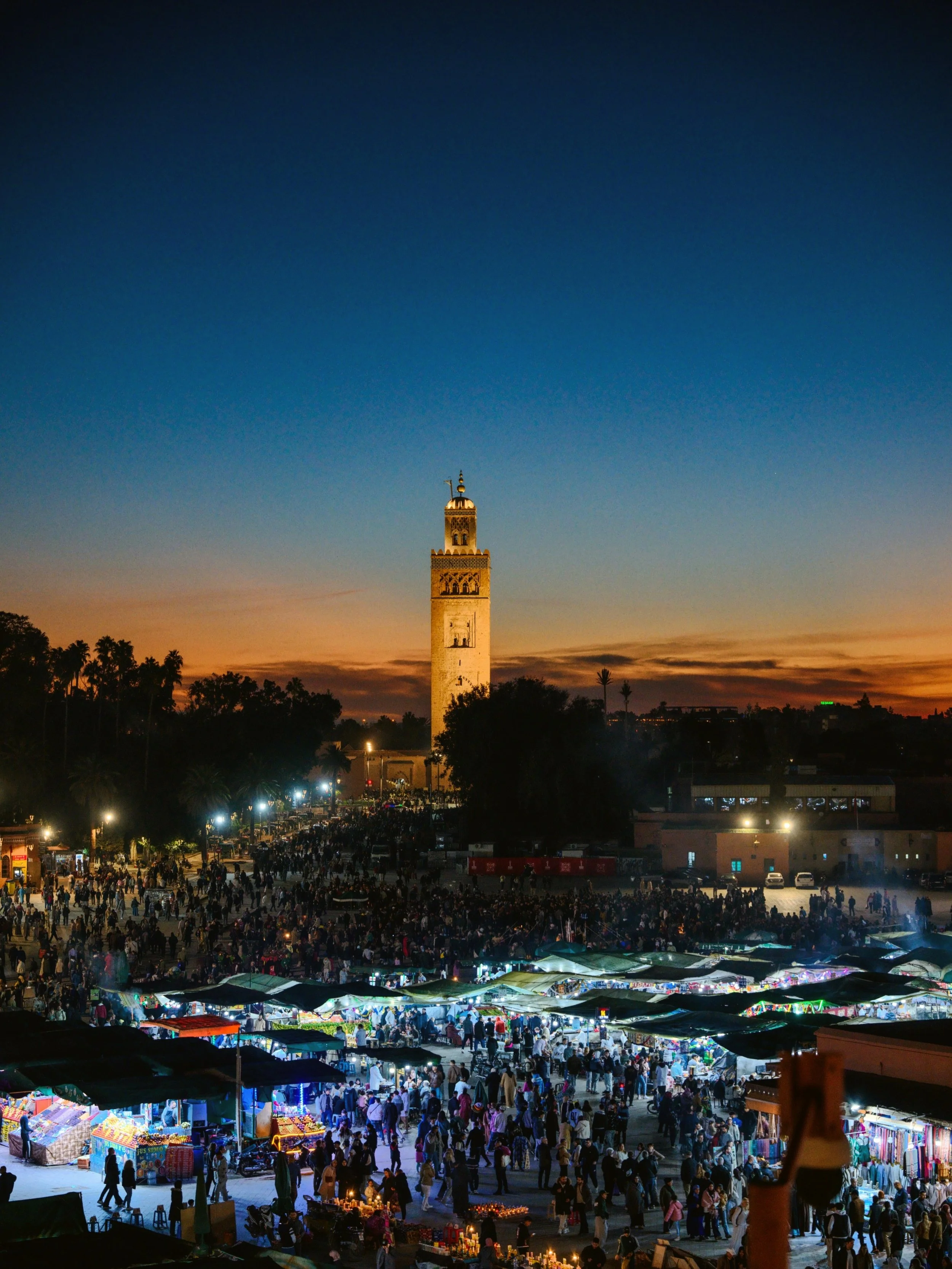 Djemaa el-Fnaa square at dusk with market stalls lit up and the Koutoubia minaret against a deep blue sky, Marrakech.
