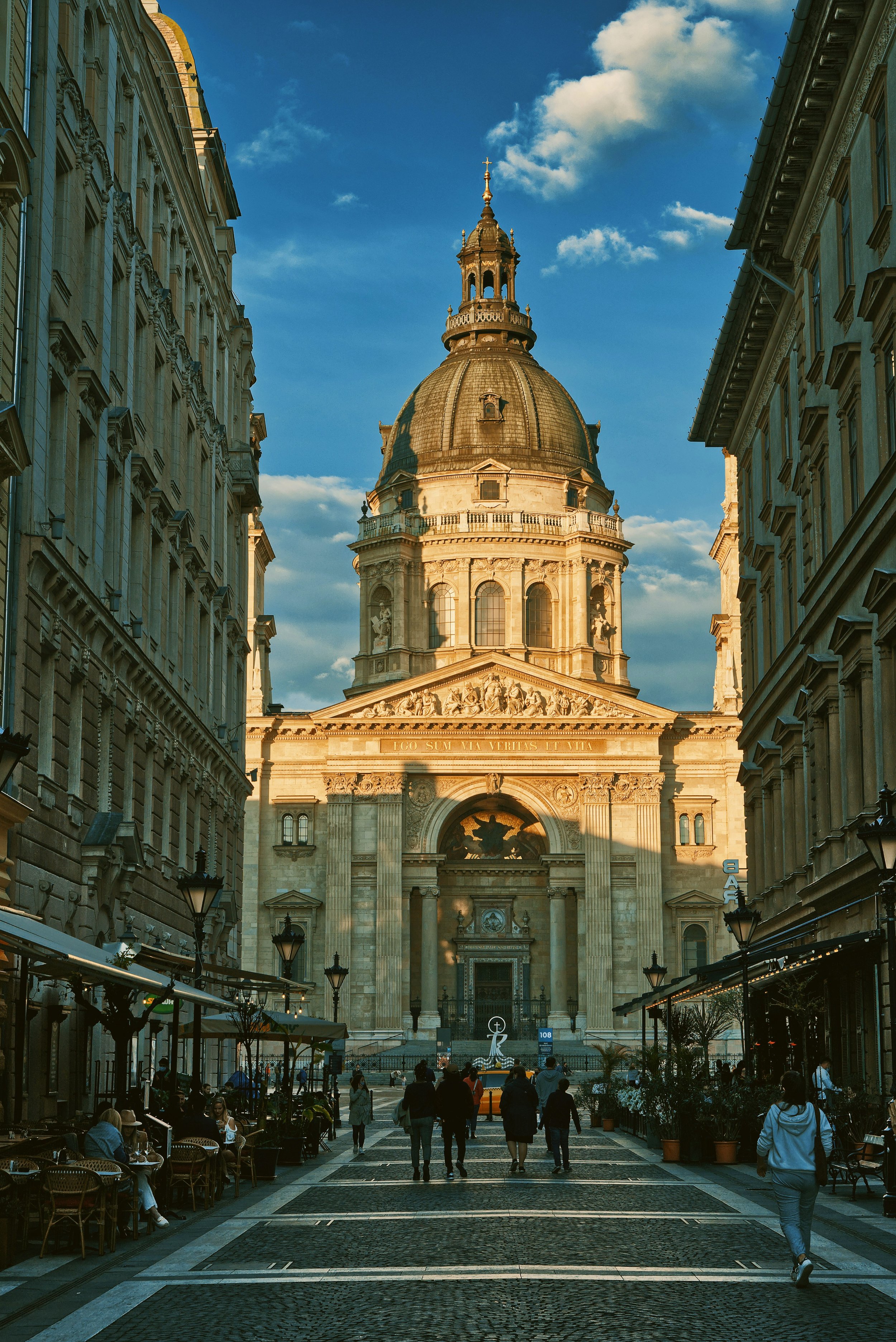 People walking toward St. Stephen's Basilica along a shaded Zrínyi street, Budapest