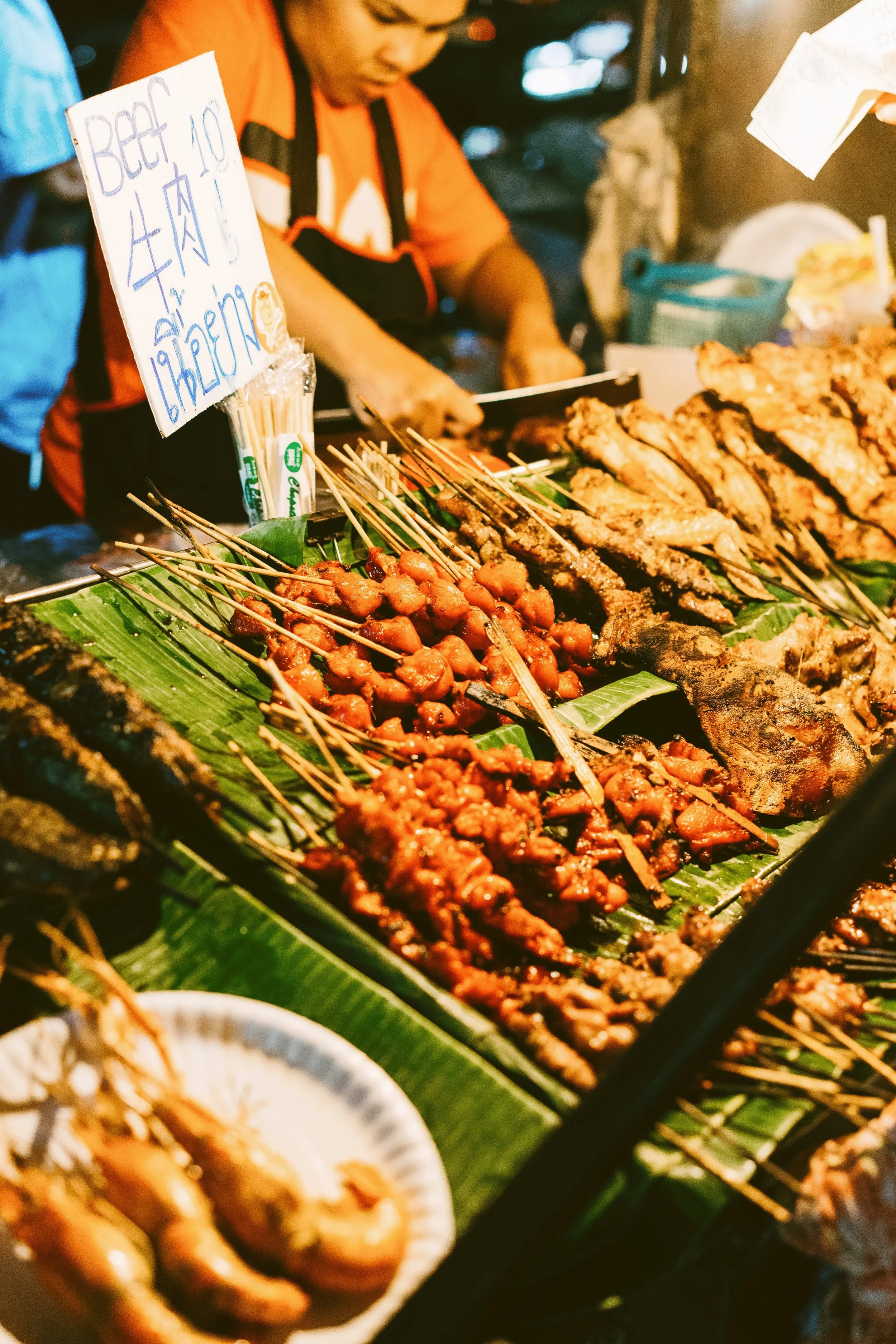 Street food stall with skewers and grilled dishes laid out on banana leaves, Bangkok.