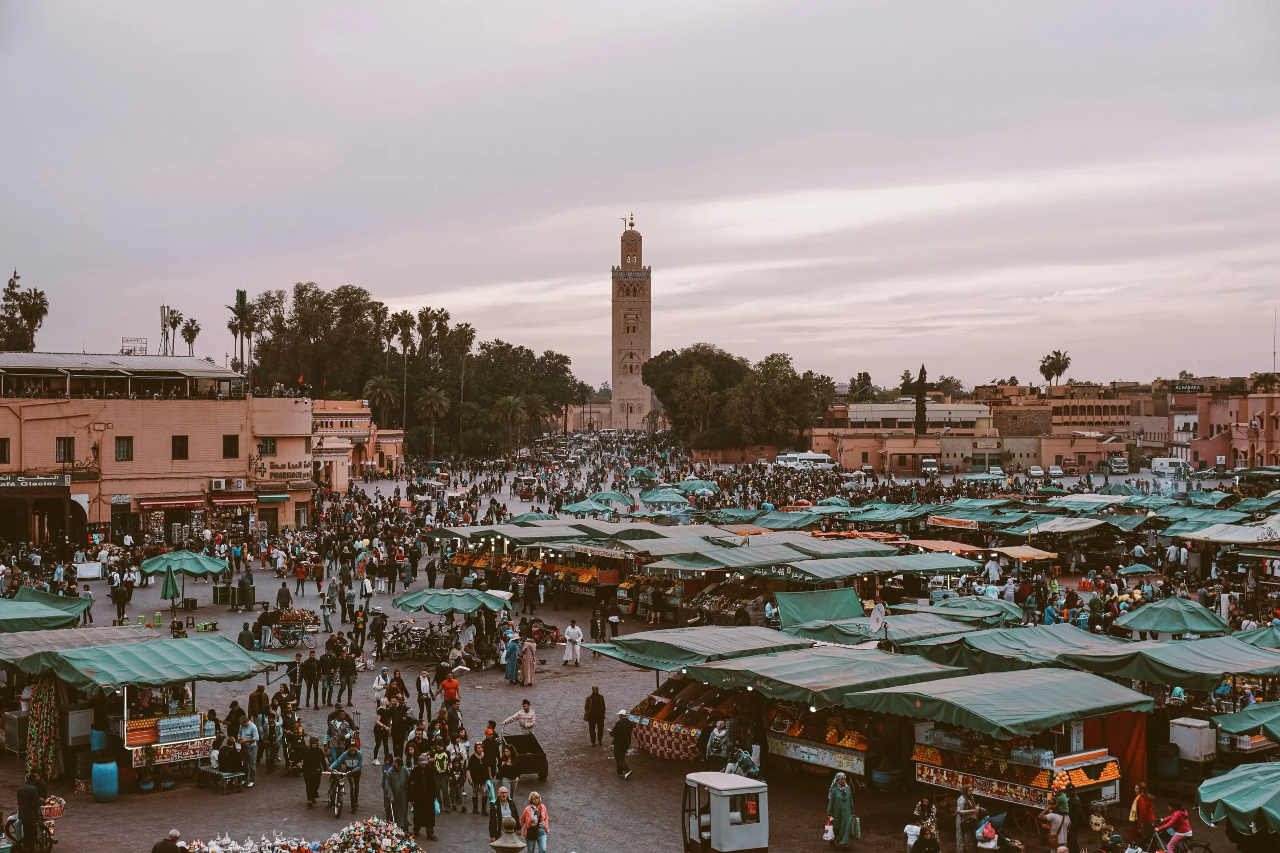 Jemaa el-Fnaa square at dusk with market stalls under green awnings and the Koutoubia minaret in the background, Marrakech.