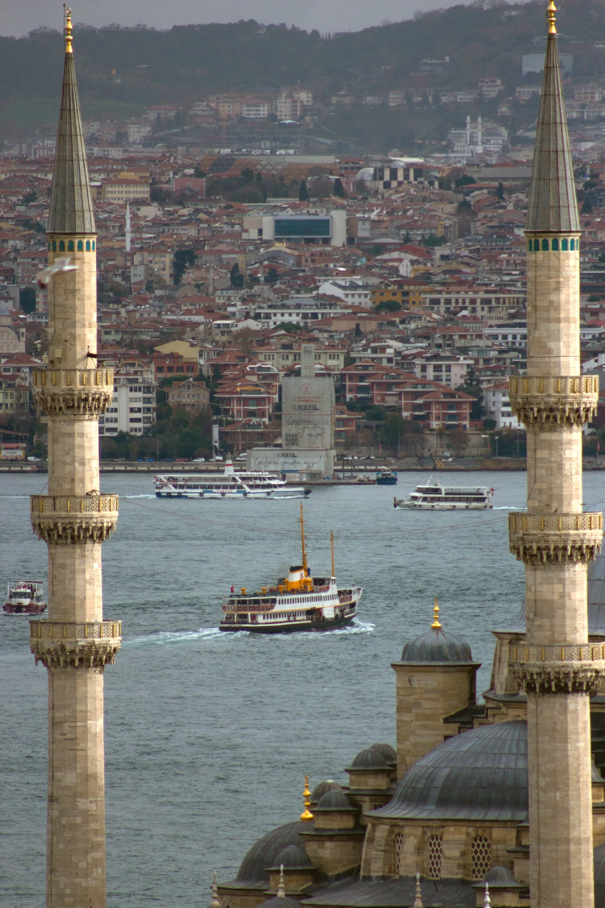 View of the Golden Horn between two minarets, with a boat on the water and the city on the hillside, Istanbul.