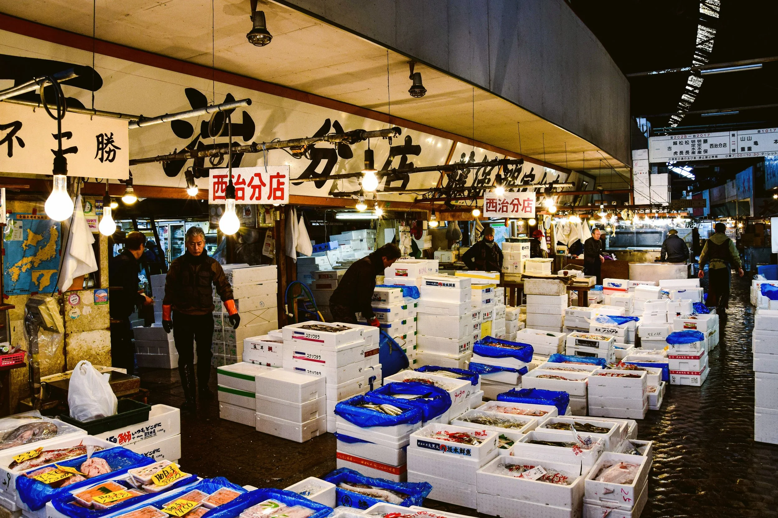 Chef in a dark uniform slicing a large fish at a market counter with onlookers behind, Tsukiji Market, Tokyo.