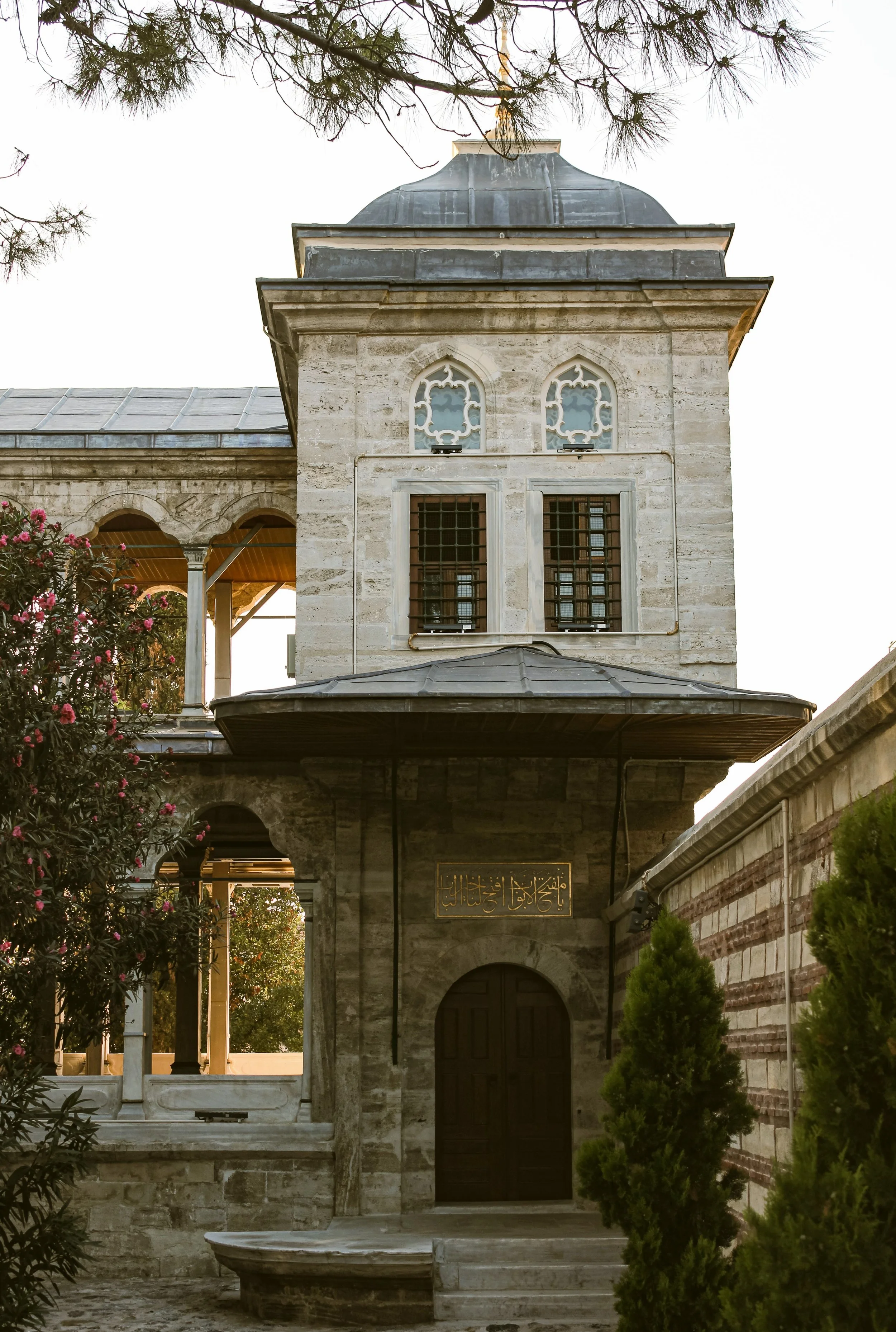 Stone tower with a gray dome and arched windows beside trees and a tiled roof, Topkapı Palace, Istanbul.