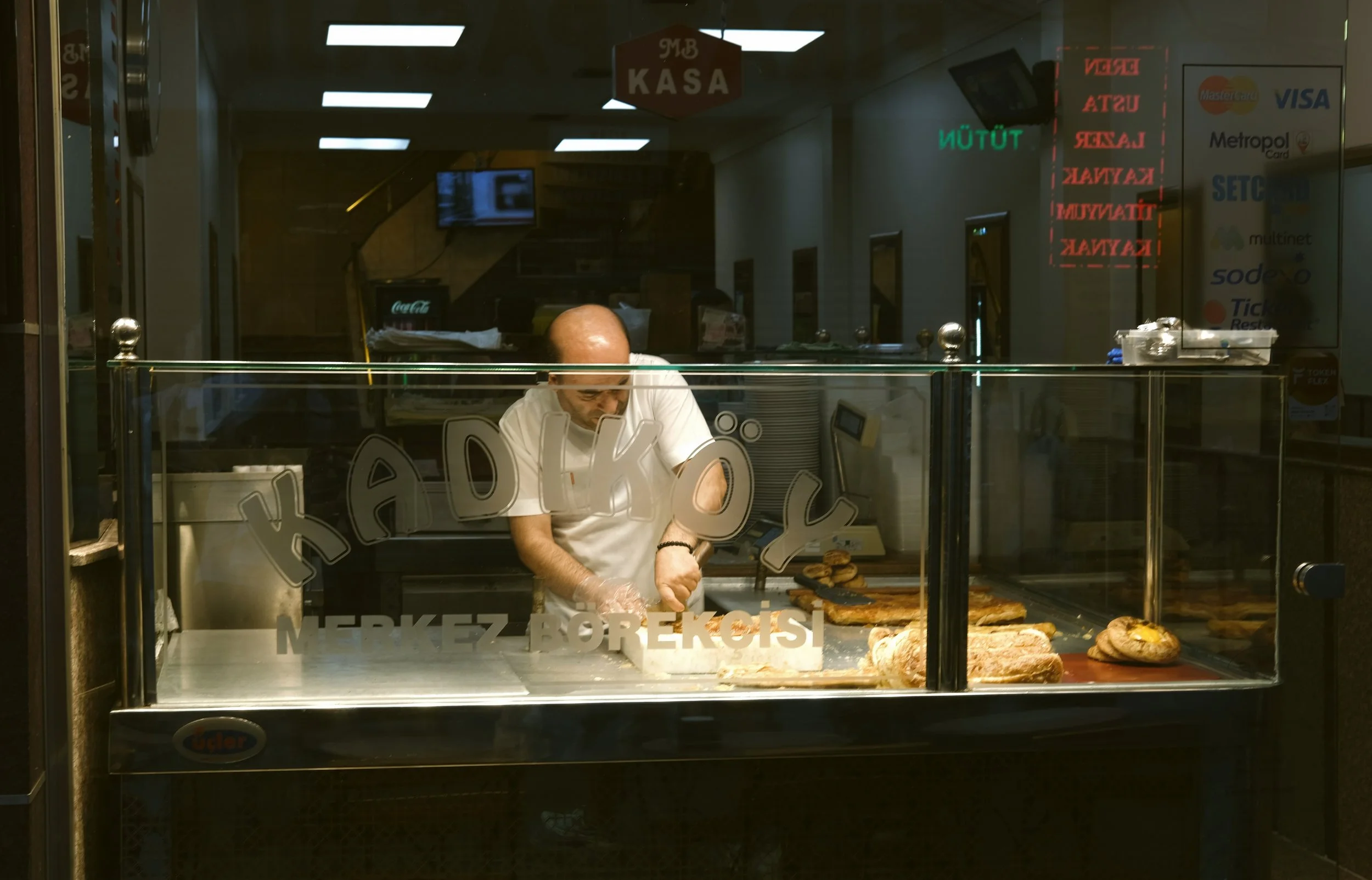 Man working behind a lit glass display counter in a bakery at night, Kadikoy, Istanbul.