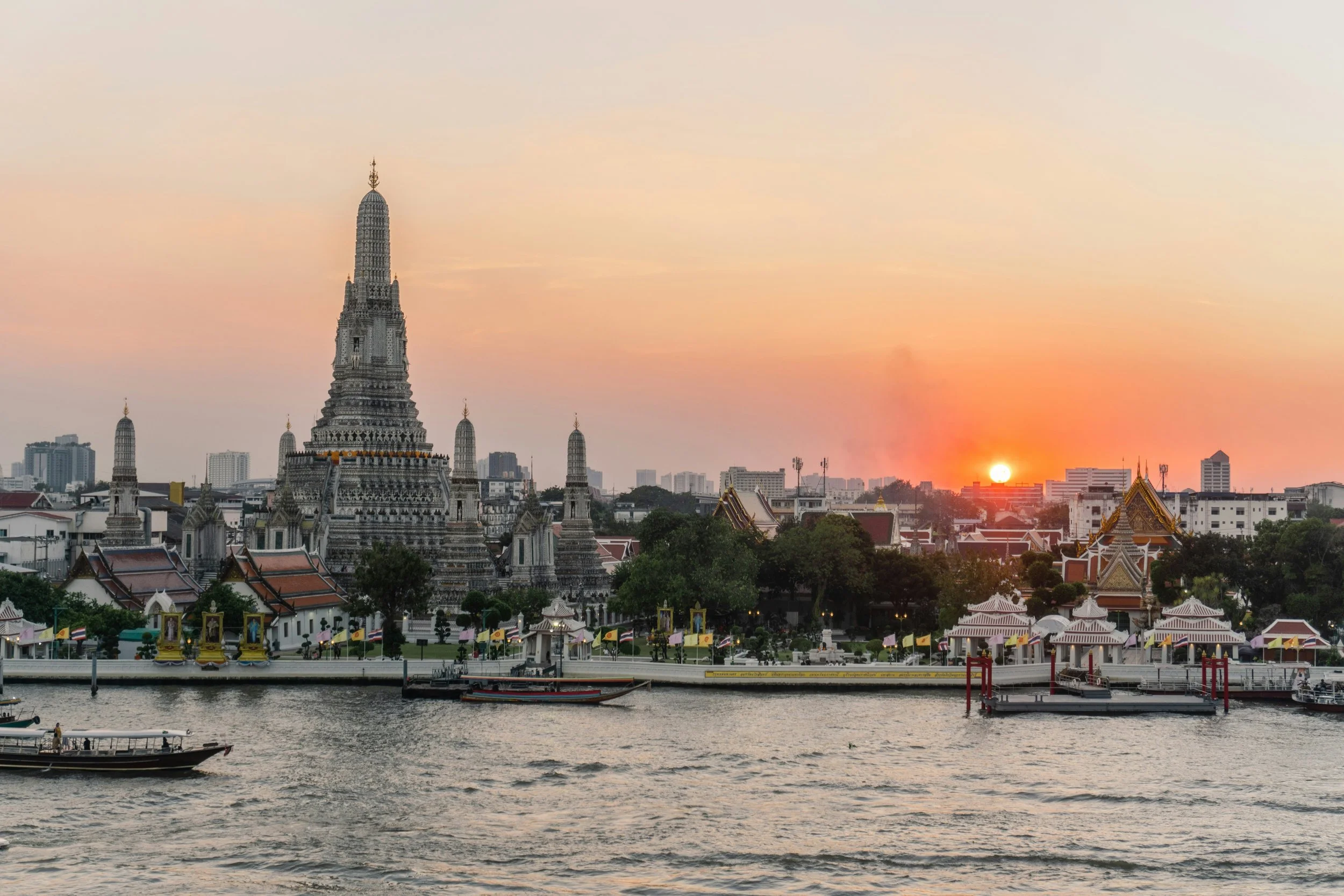 Wat Arun temple silhouetted at sunset across the Chao Phraya River, Bangkok.