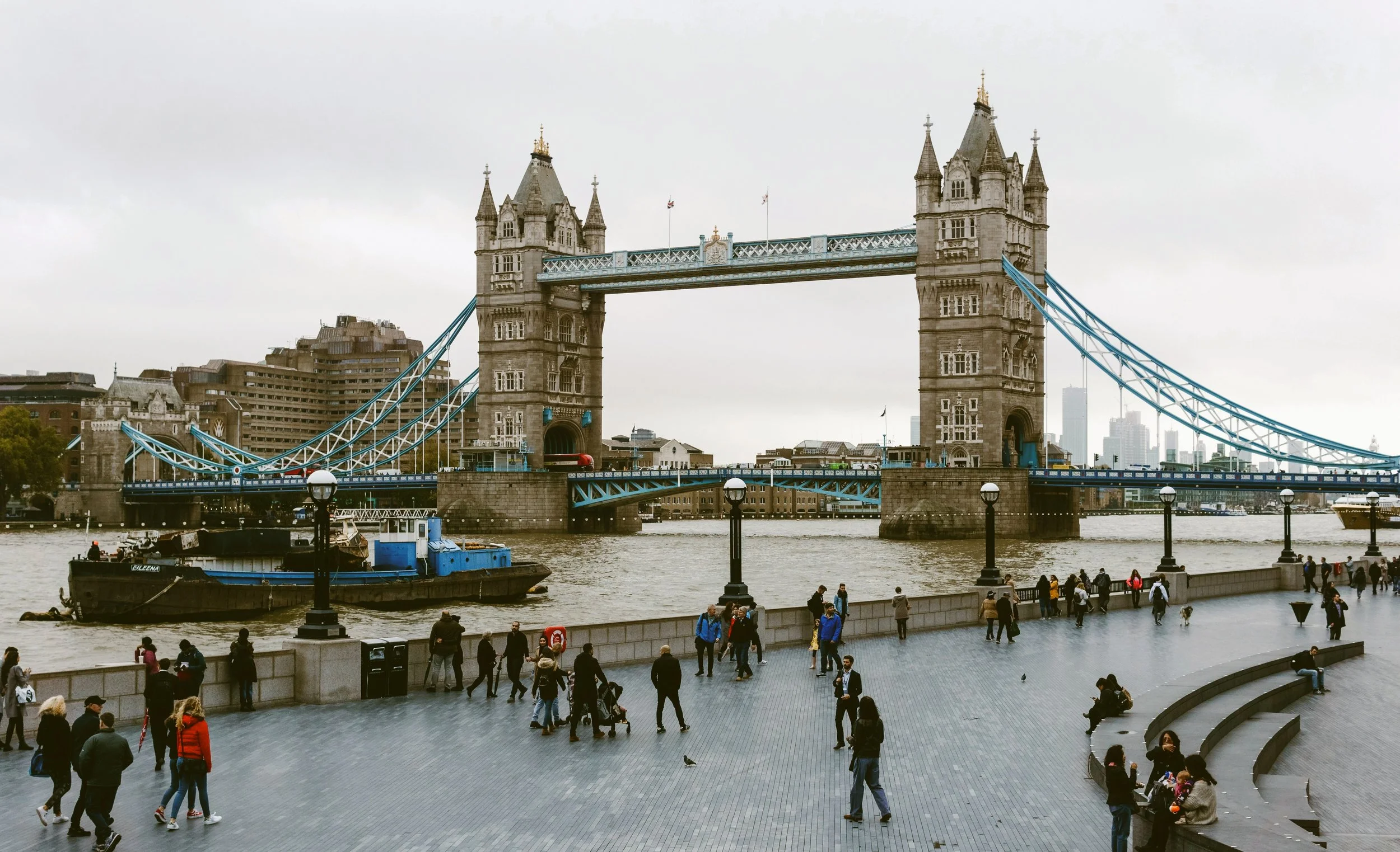 Tower Bridge with its twin towers rising above the River Thames and crowds walking below, in London