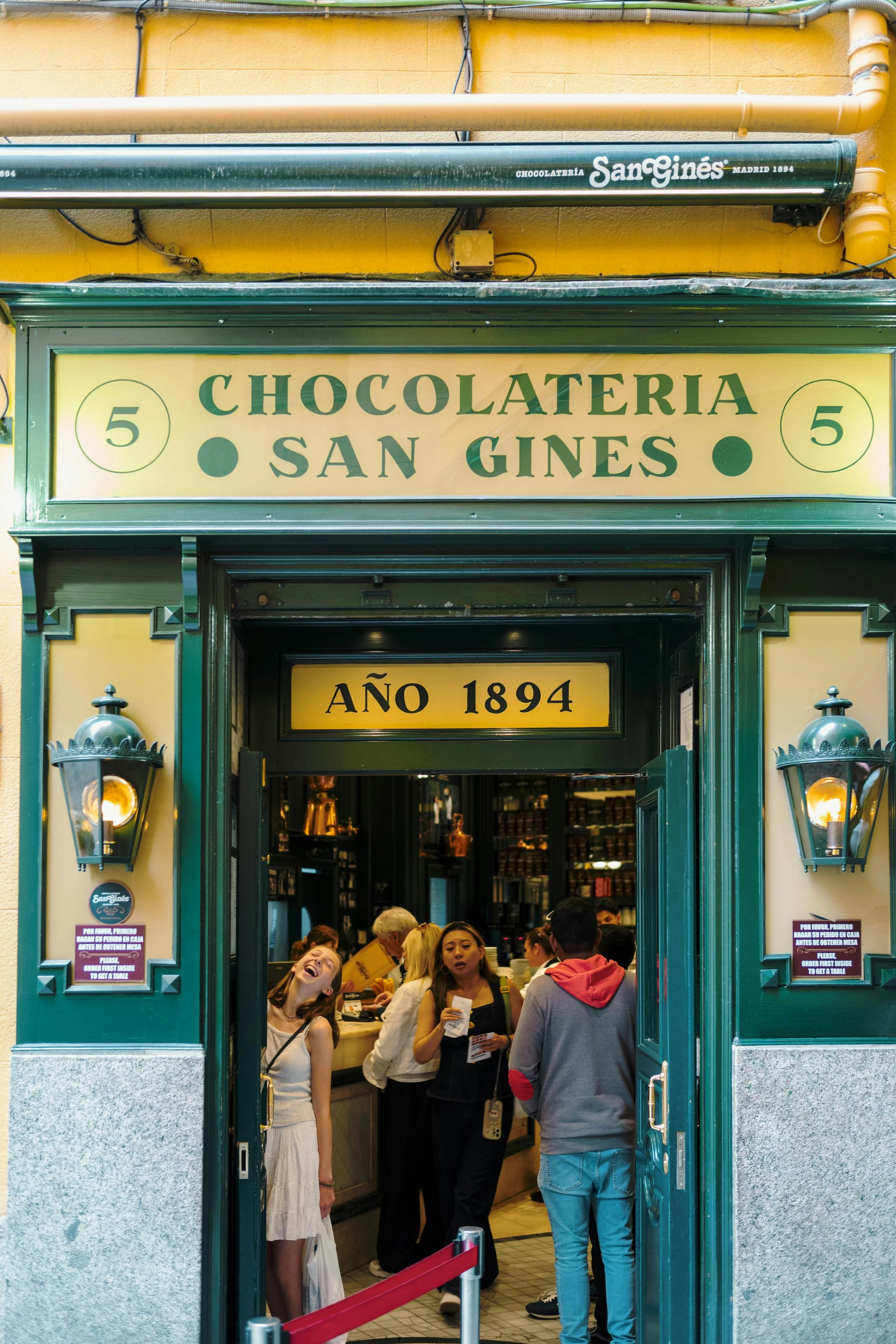Green and yellow facade of Chocolatería San Ginés with people at the entrance, Madrid