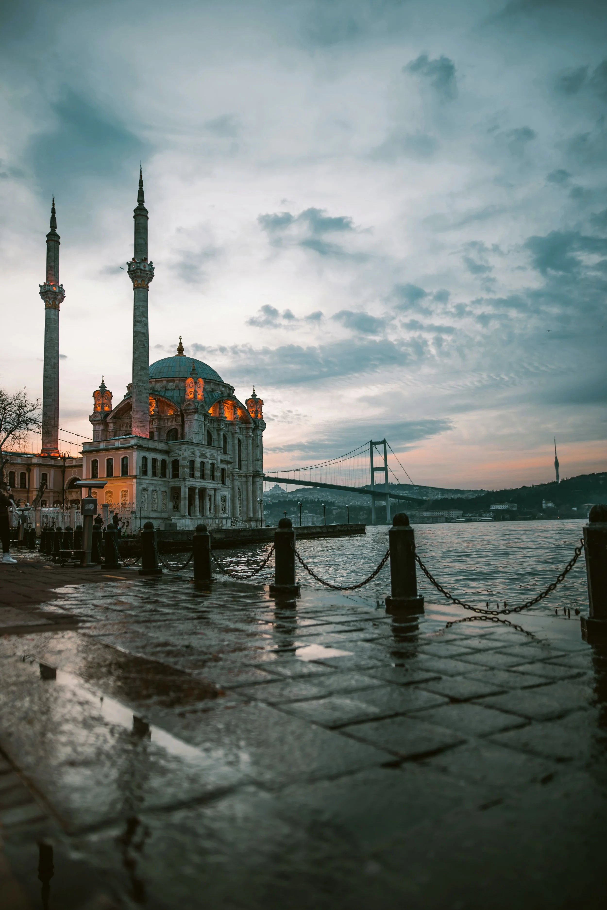Ortaköy Mosque beside the Bosphorus under a stormy sky, with wet stone paving in the foreground, Istanbul.
