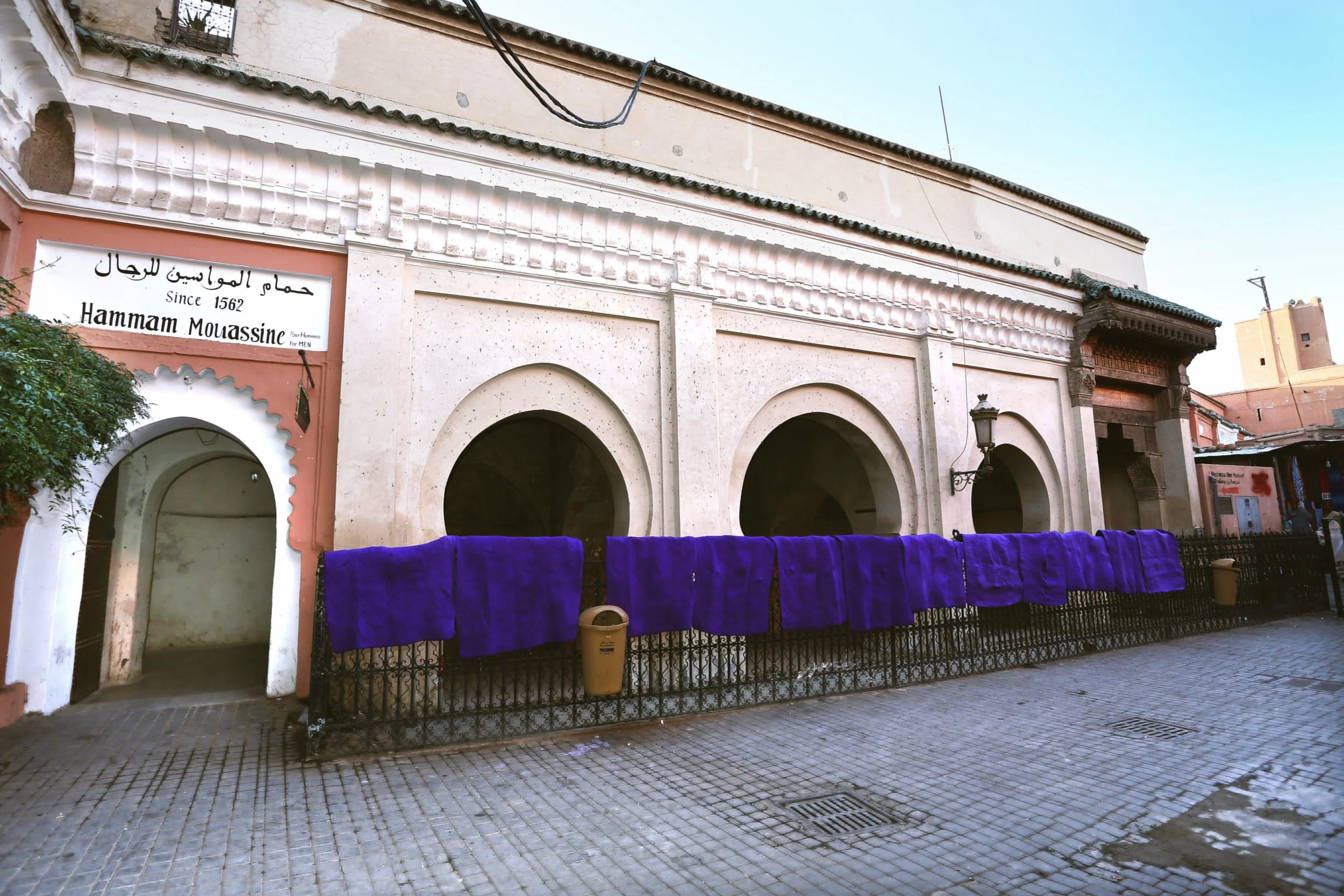 Hammam Mouassine facade with arched doorways and purple flowers along the wall, Marrakech.
