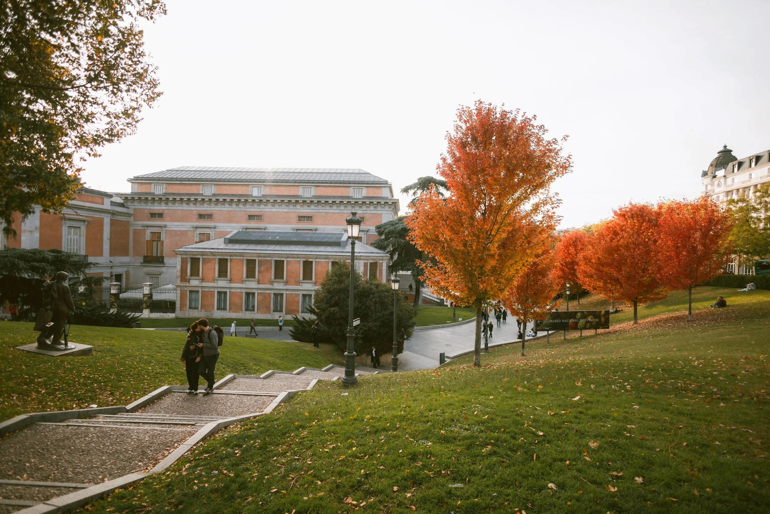 Historic Museo del Prado building behind a grassy slope and autumn foliage, Madrid