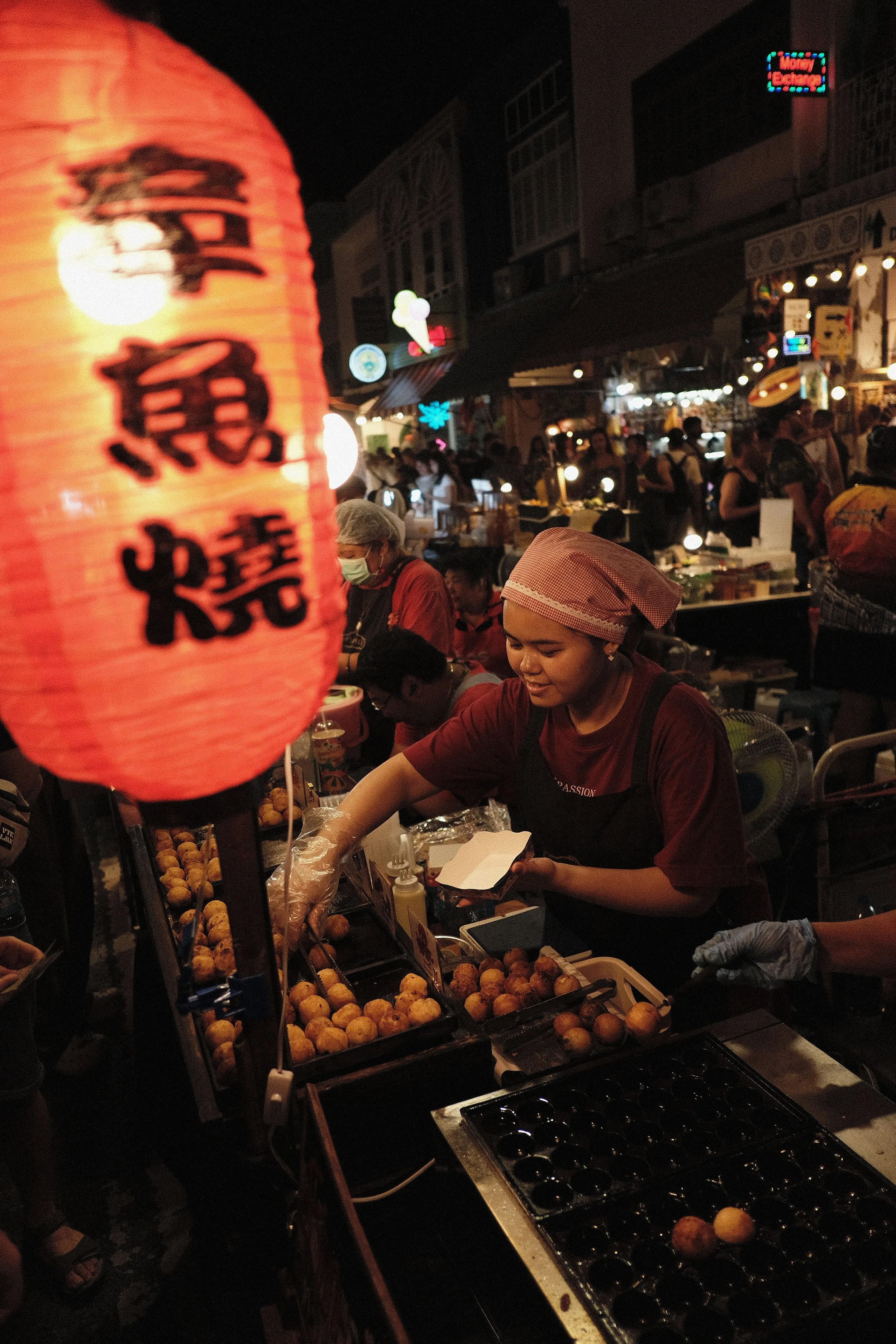 Red paper lantern with Chinese characters above a diner eating at an outdoor stall at night, Bangkok.