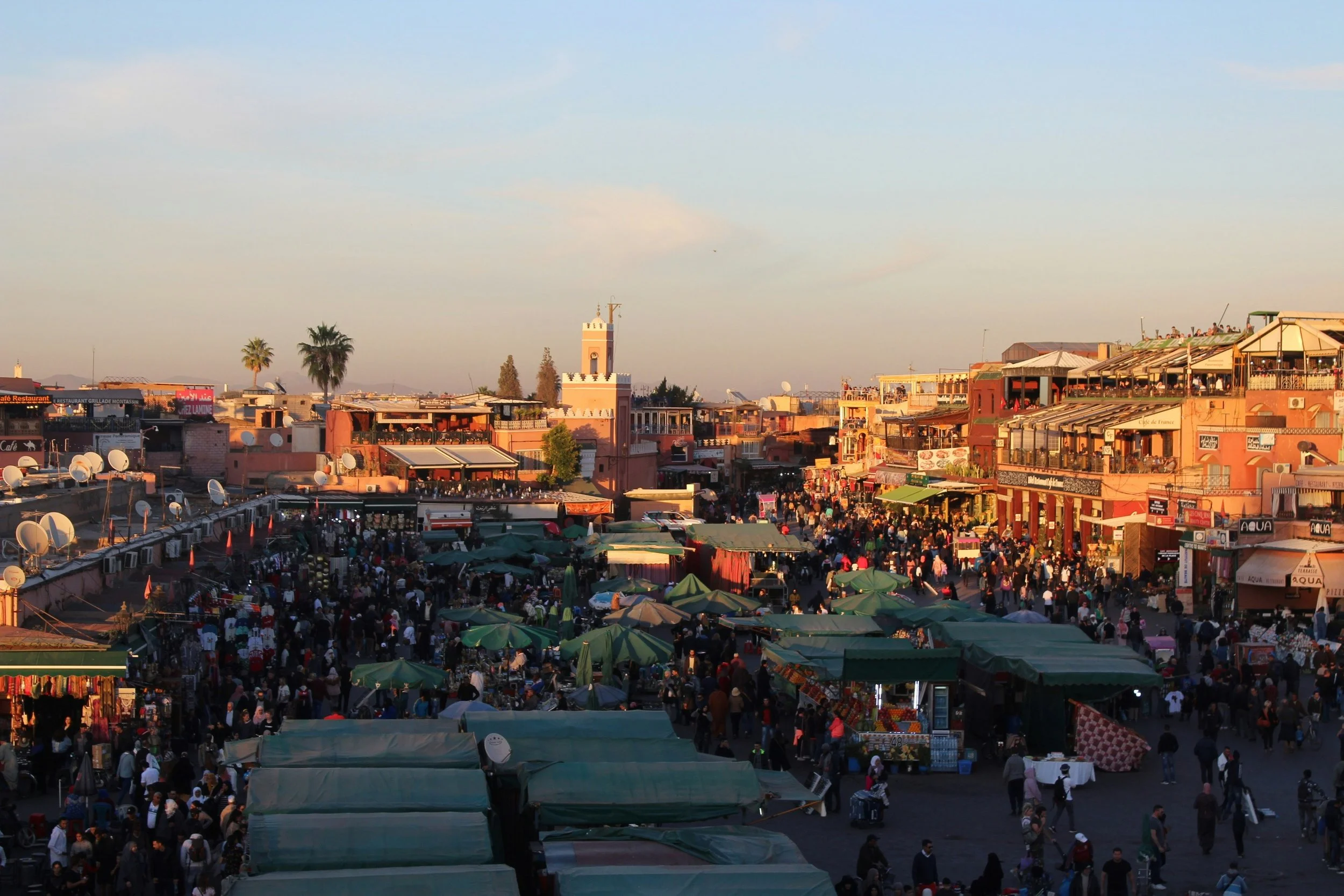 Rooftop view over the Marrakech medina at sunset, with market stalls below and minarets on the horizon, Marrakech.