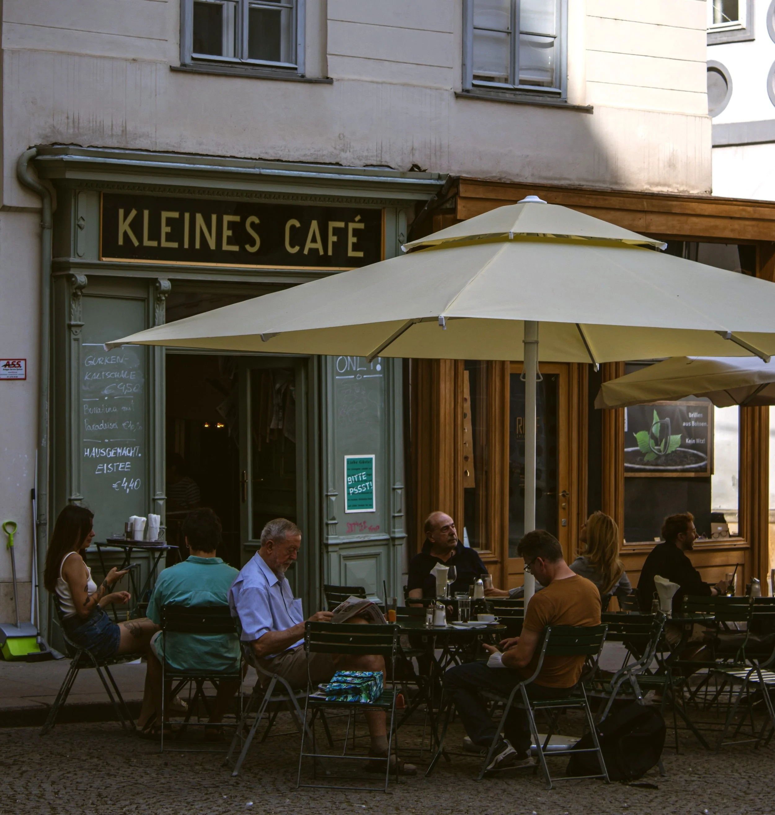 People seated at an outdoor Viennese coffeehouse terrace beneath green awnings.