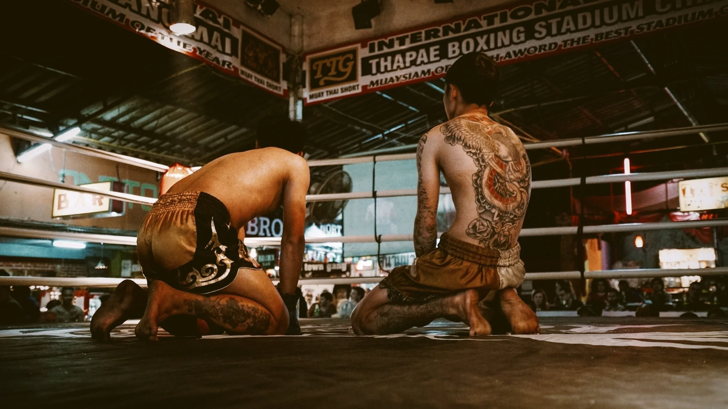 Two Muay Thai fighters are kneeling in a boxing ring, preparing for a match, Bangkok.