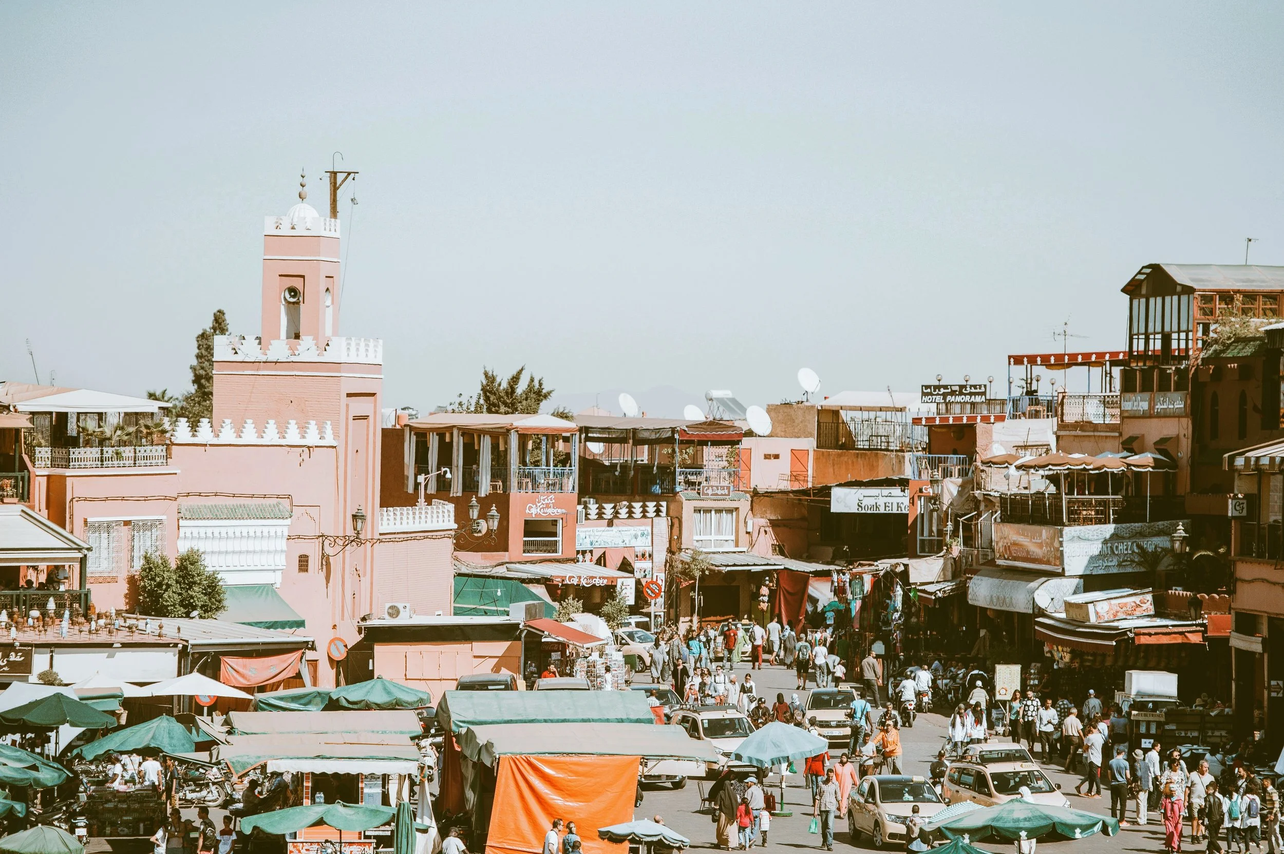 Rooftop view over a market square with a pink minaret and colorful stalls below, Marrakech.