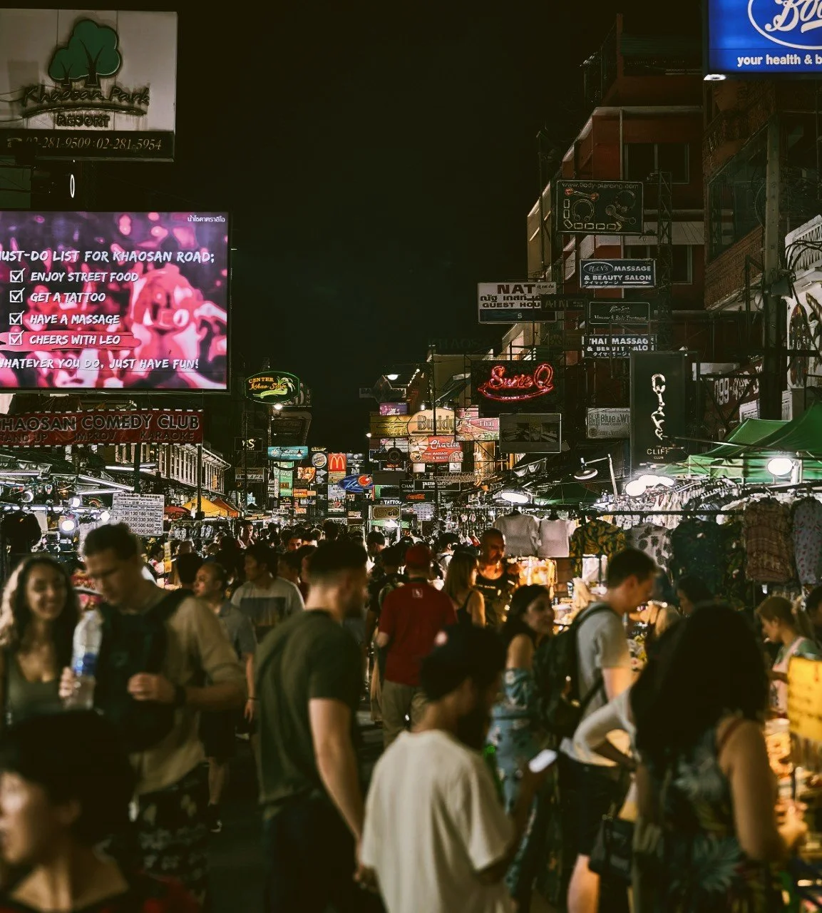 Crowds of people walking along a busy street at night lit by neon signs, Khao San Road, Bangkok.
