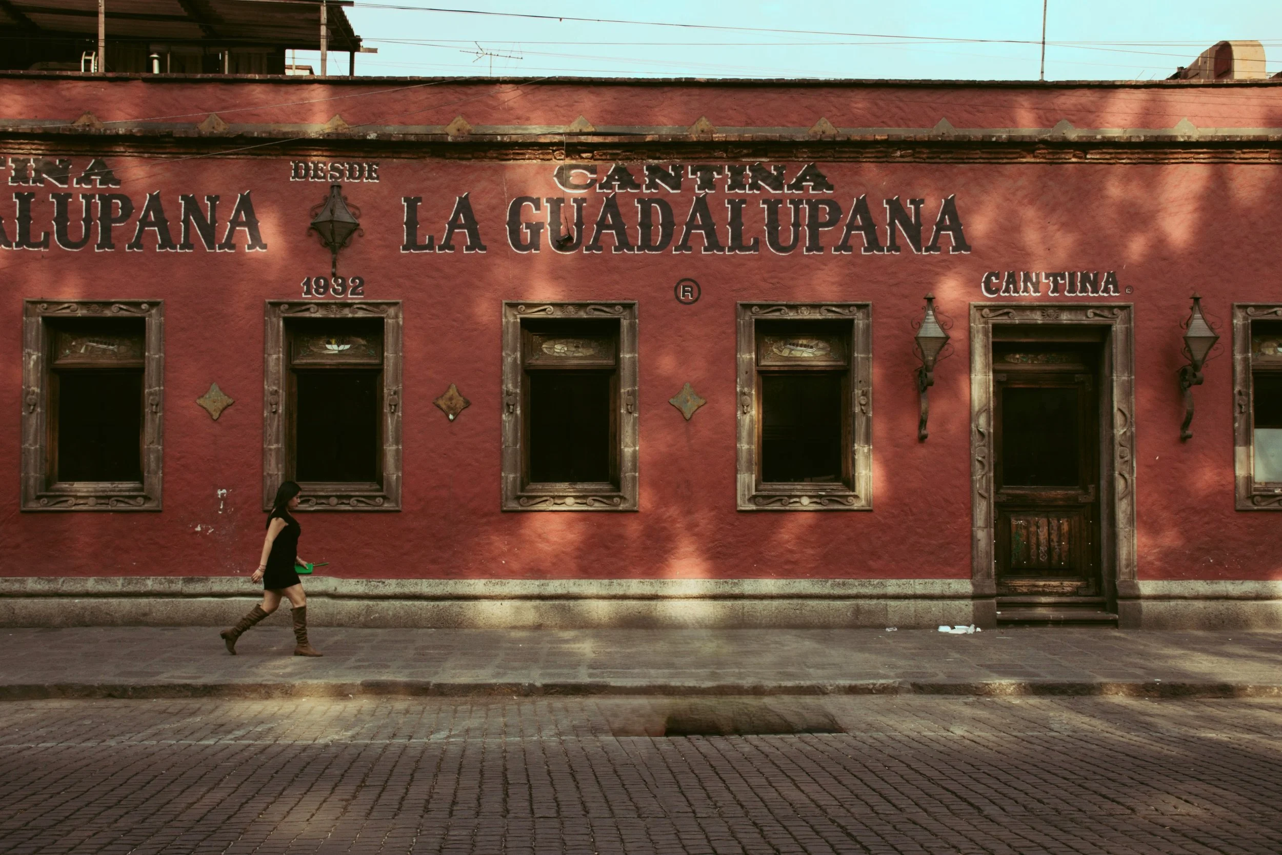 Red cantina facade with a sign reading La Guadalupana and a person walking along the sidewalk, Mexico City.