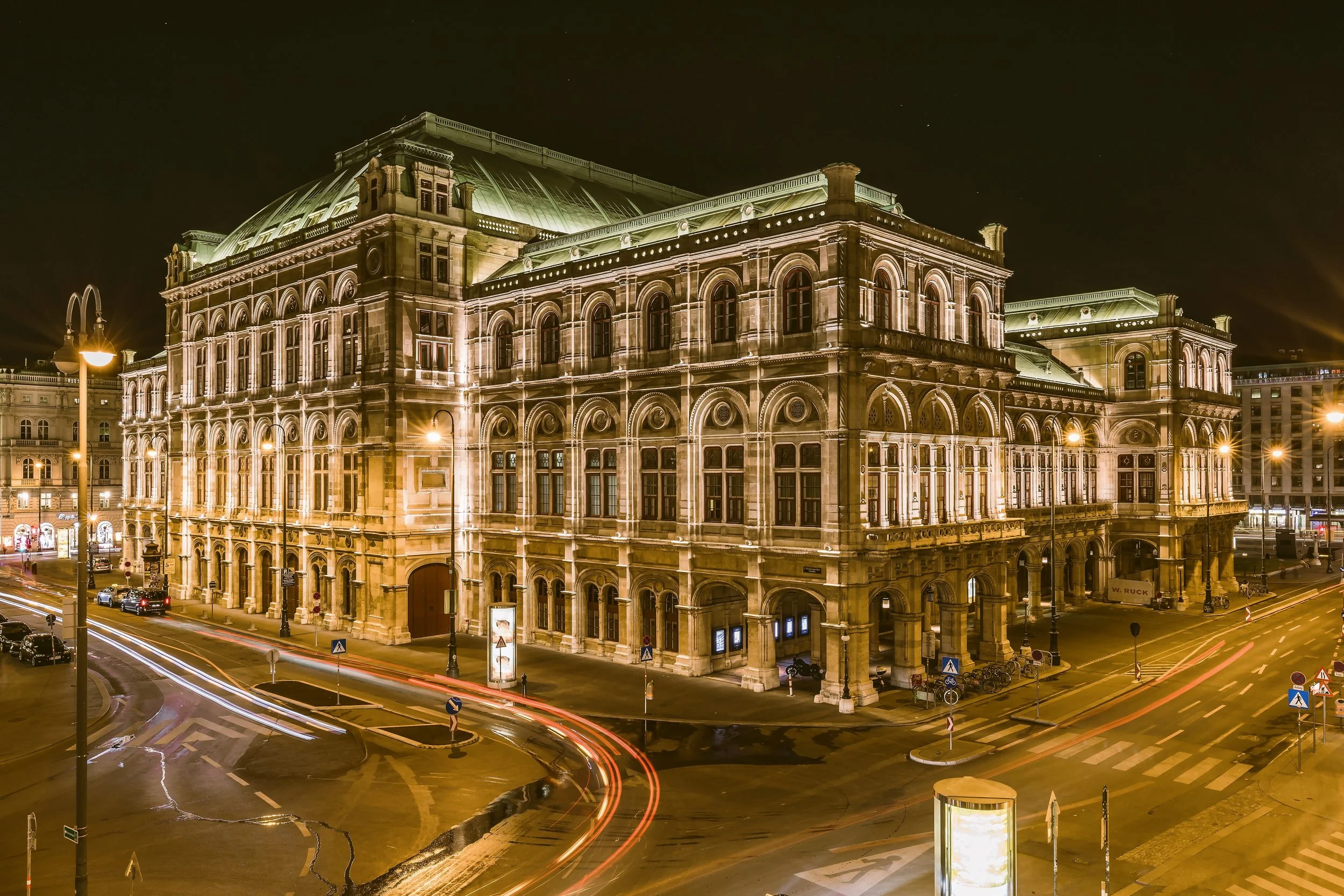 Vienna State Opera illuminated at night with light trails from passing cars on the street in front, Vienna