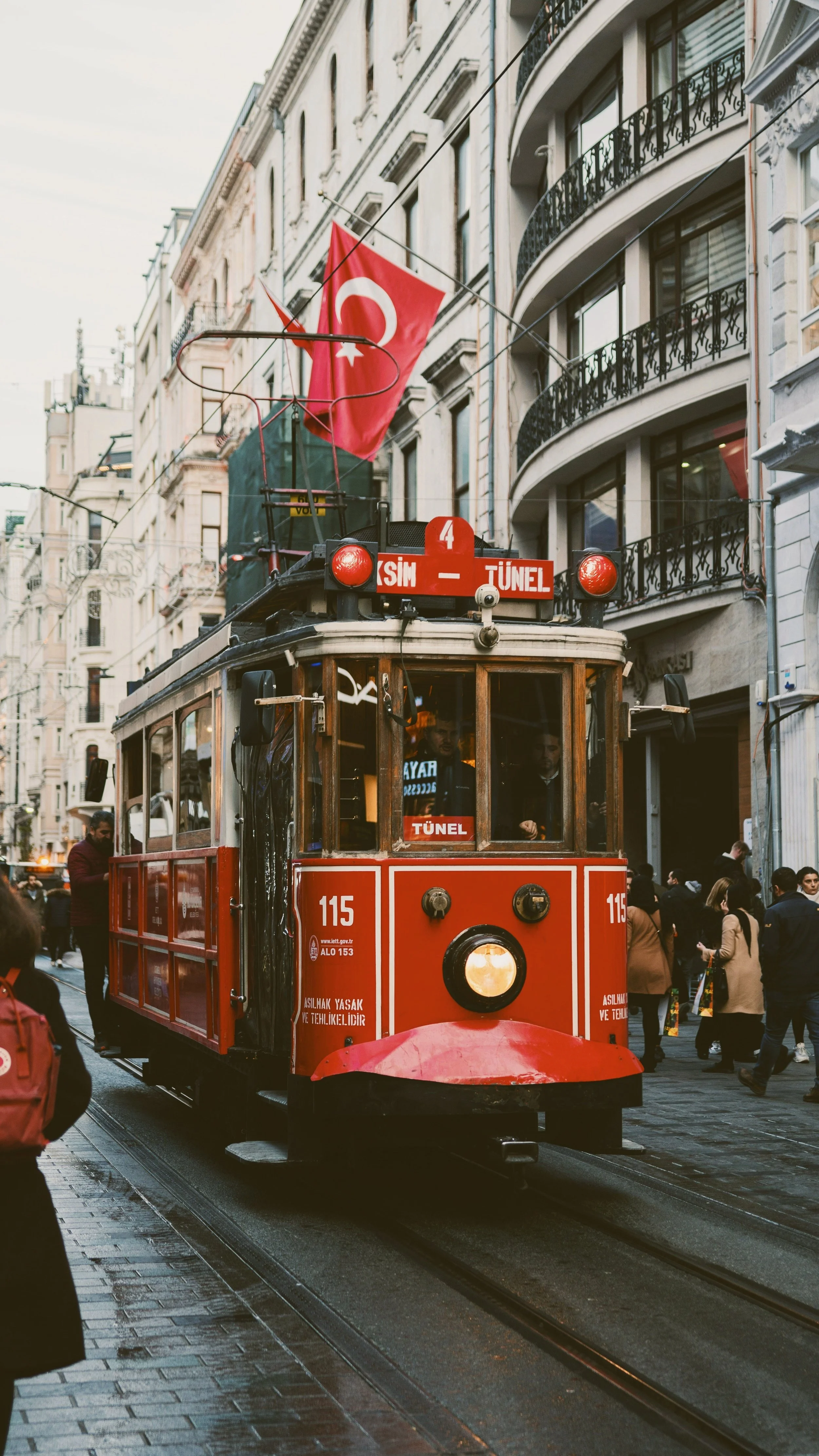 Red vintage tram on a wet city street lined with buildings, Istiklal Avenue, Istanbul.