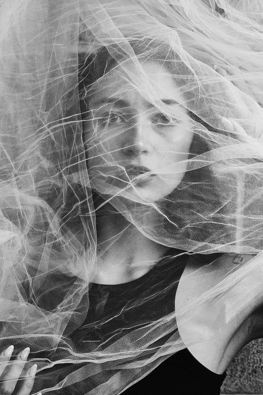 Retrato artístico de uma mulher com cabelo escuro, envolvendo-se em uma cortina de seda transparente, em preto e branco.