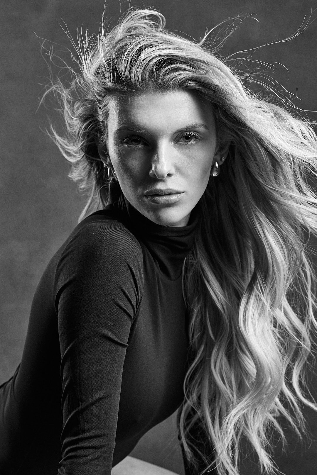 Retrato em preto e branco de uma mulher com cabelo ondulado e loiro, usando uma roupa de mangas compridas, olhando para a câmera com expressão séria