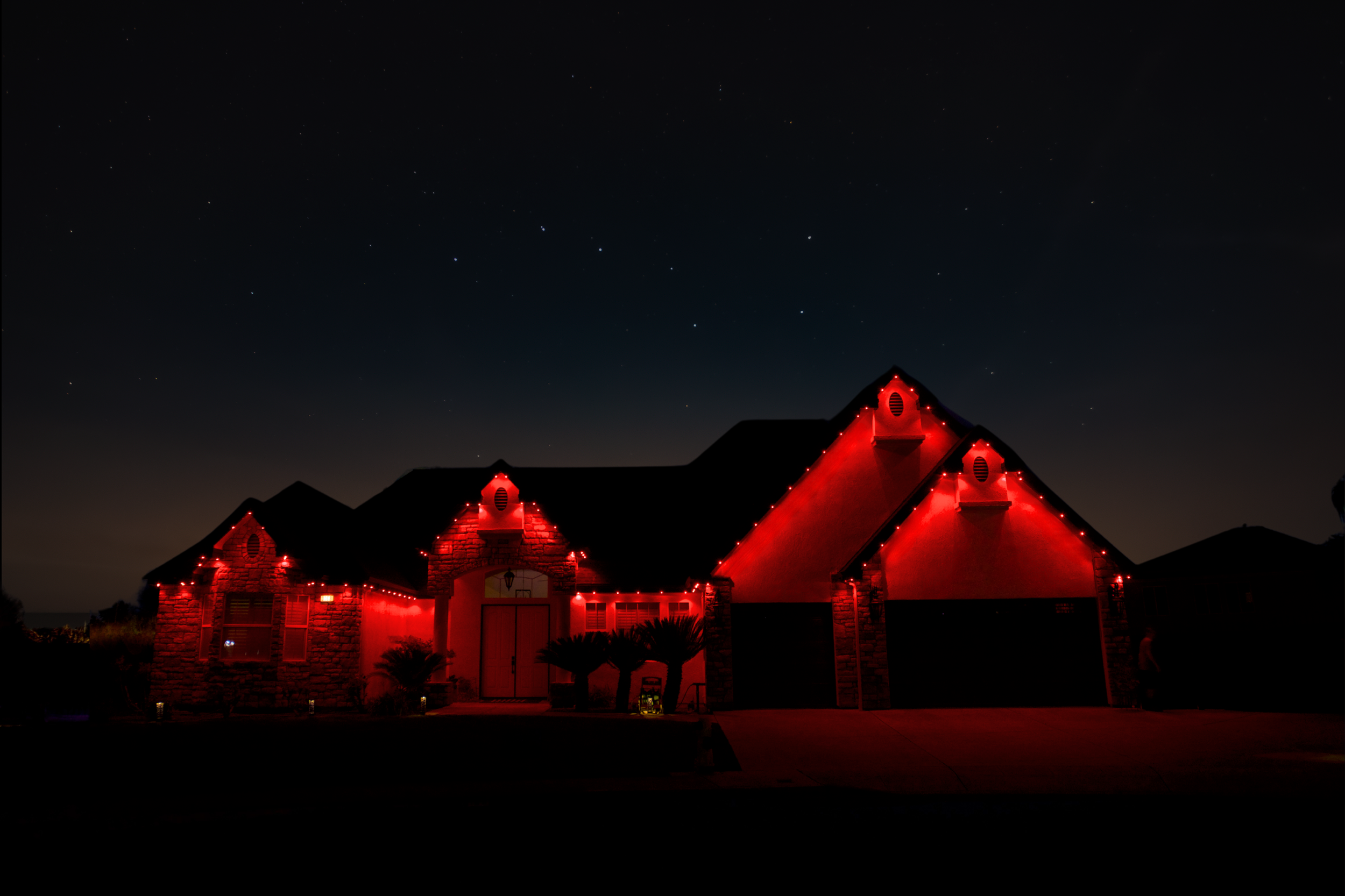 House decorated with red Christmas lights at night, with stars visible in the dark sky above.